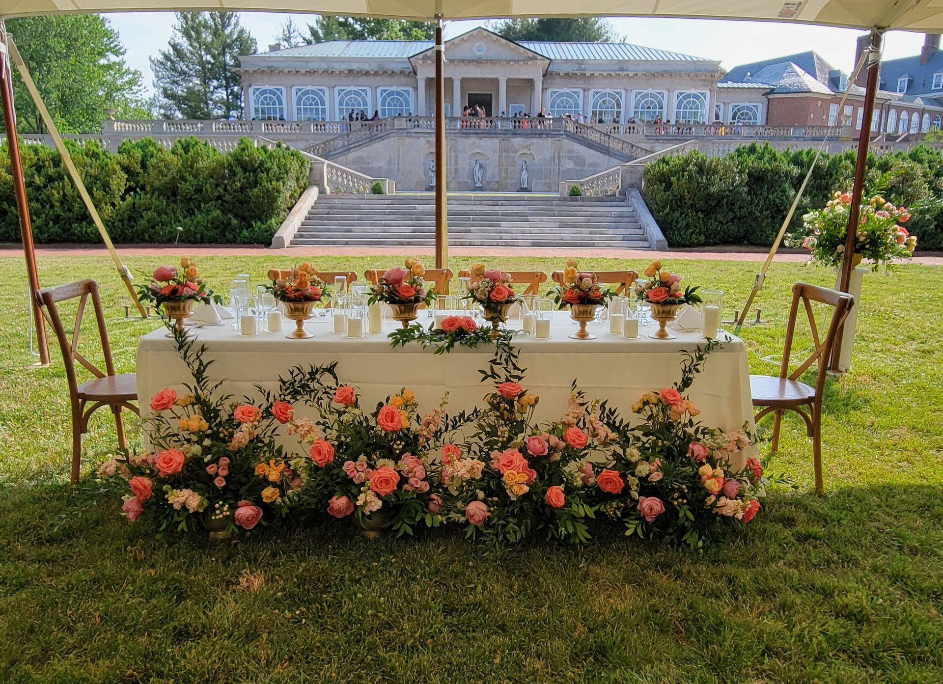 A long table with flowers on it under a tent in the grass.