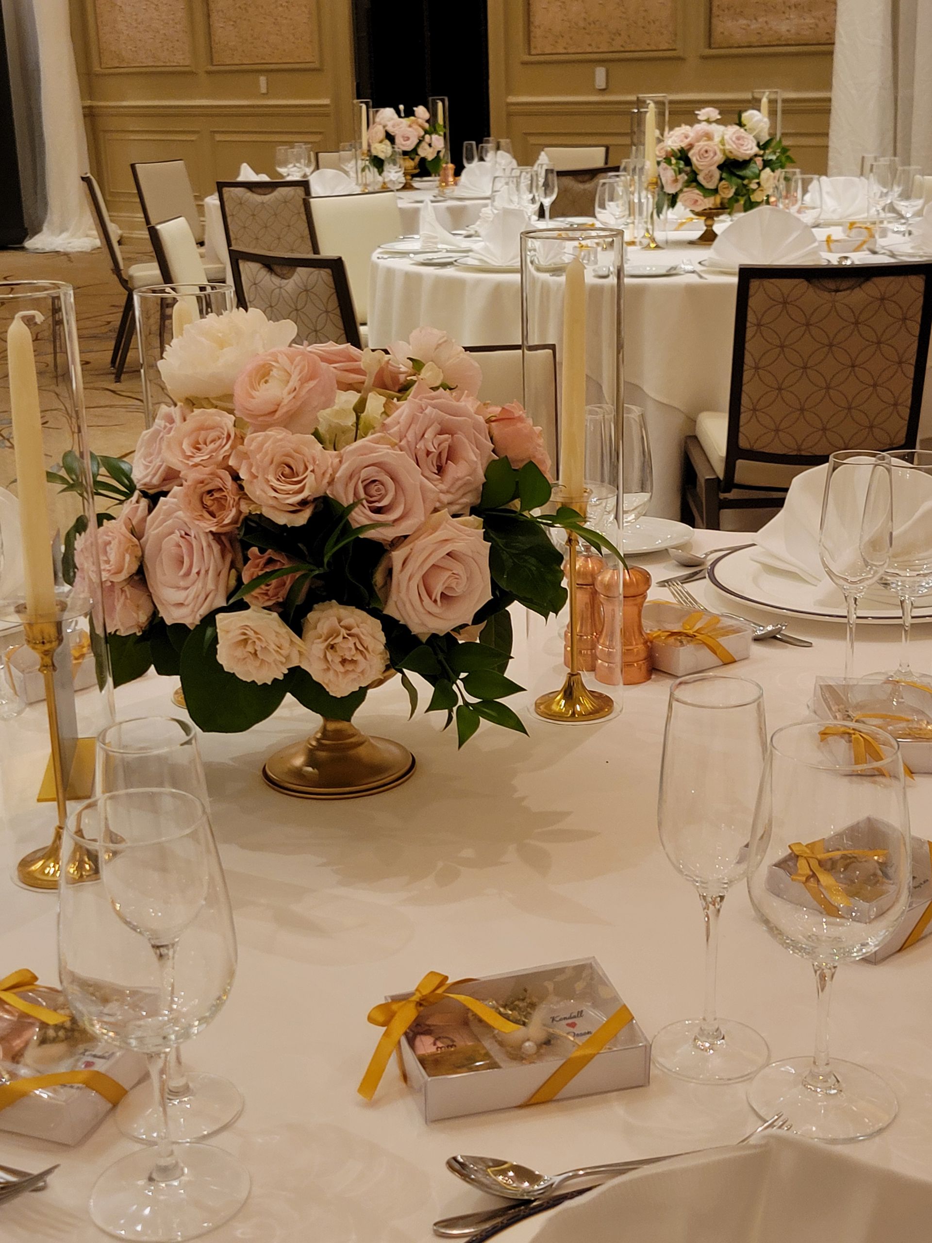 A table set for a wedding reception with a vase of pink roses on it.