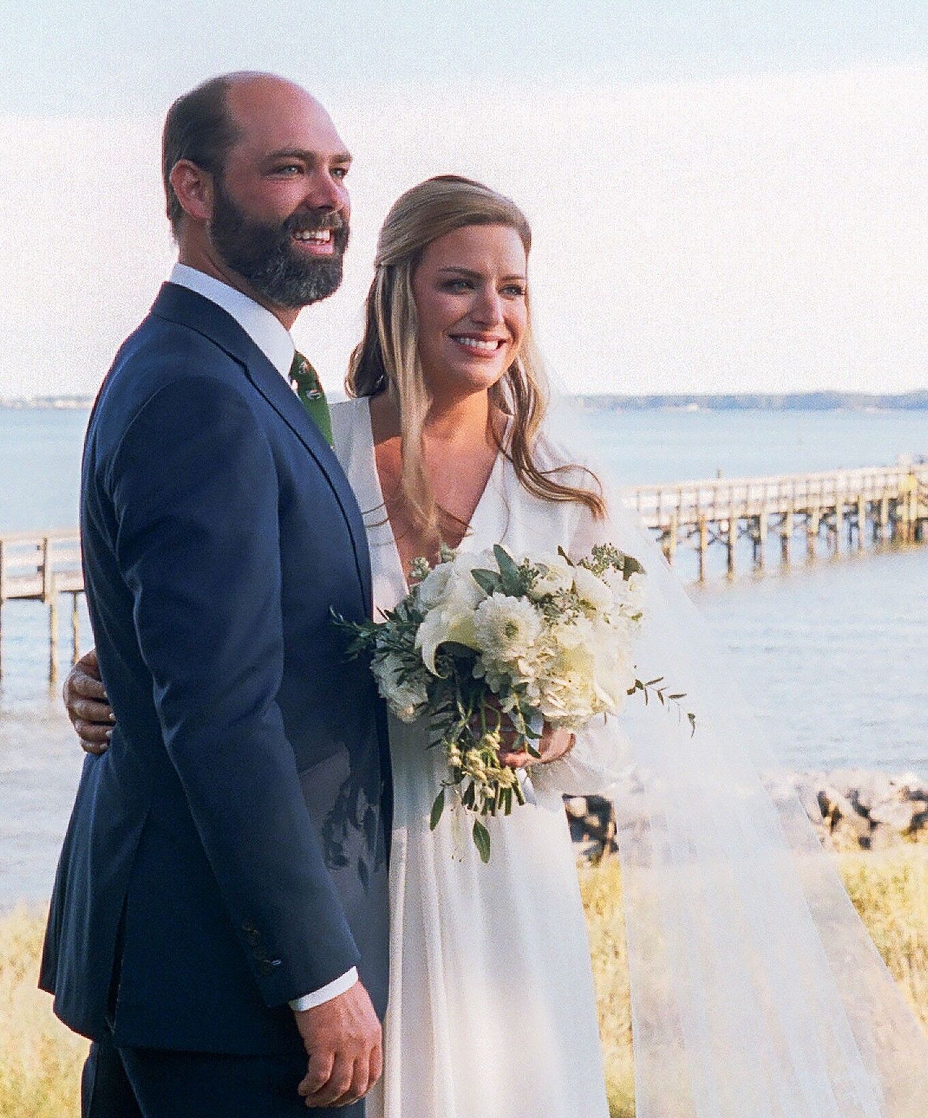 A bride and groom are posing for a picture in front of the ocean.