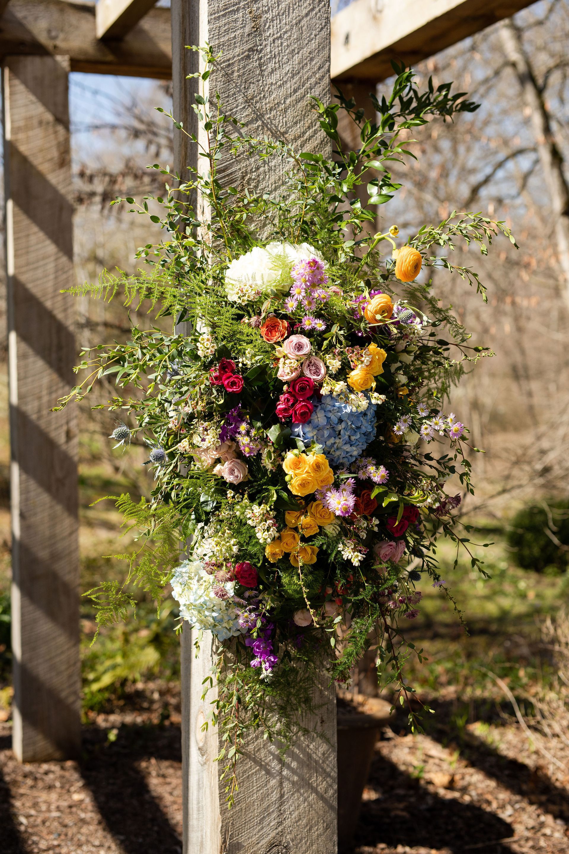 A large bouquet of flowers is hanging from a wooden pergola.