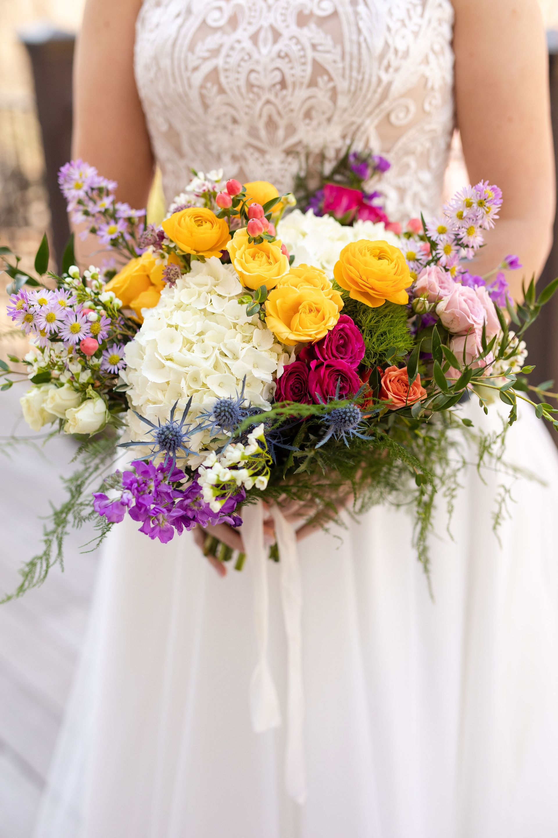 A bride in a white dress is holding a bouquet of colorful flowers.