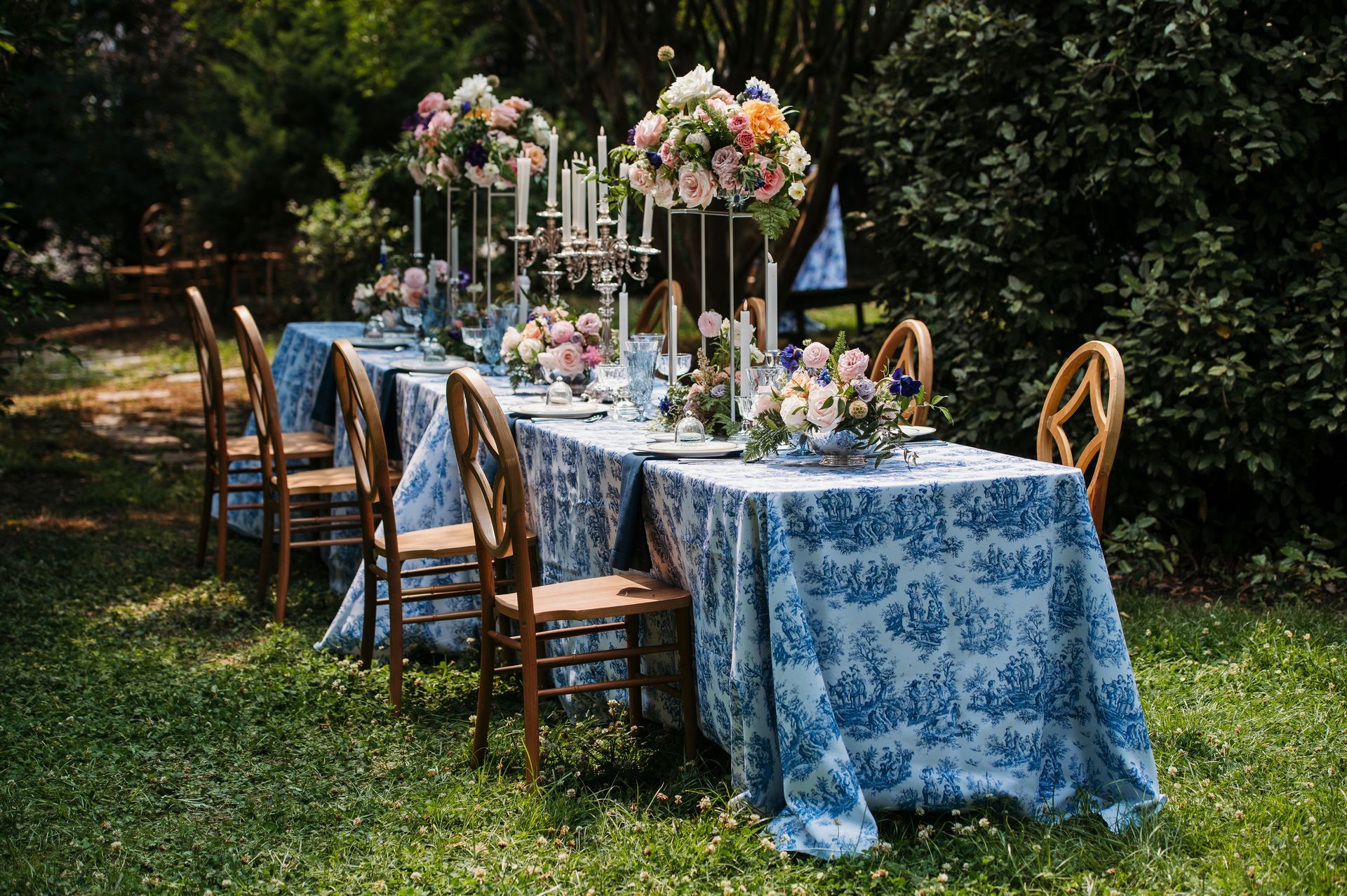 A long table with a blue and white tablecloth is sitting in the grass.