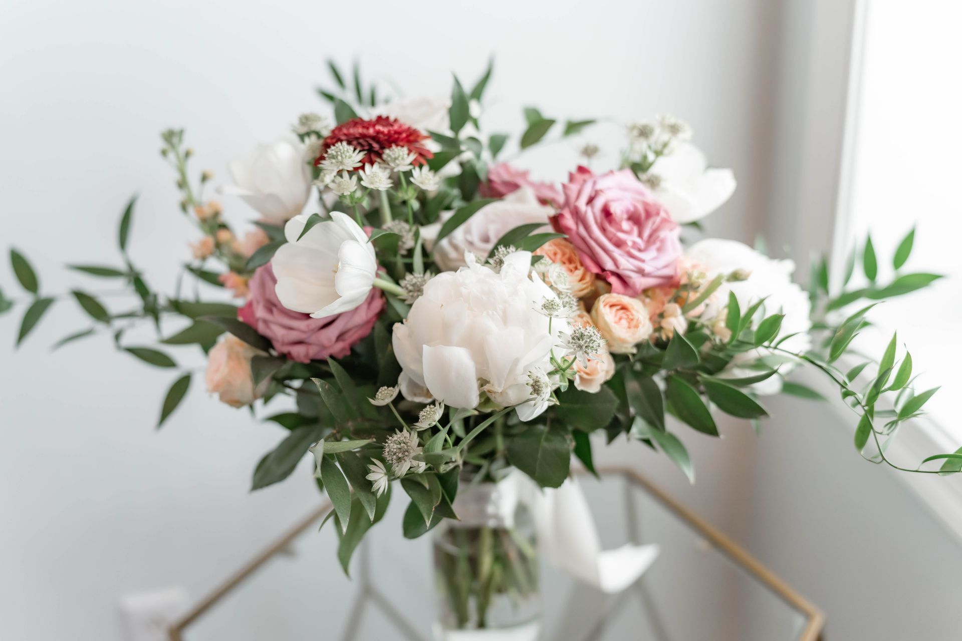 A bouquet of flowers is sitting on a table in front of a window.