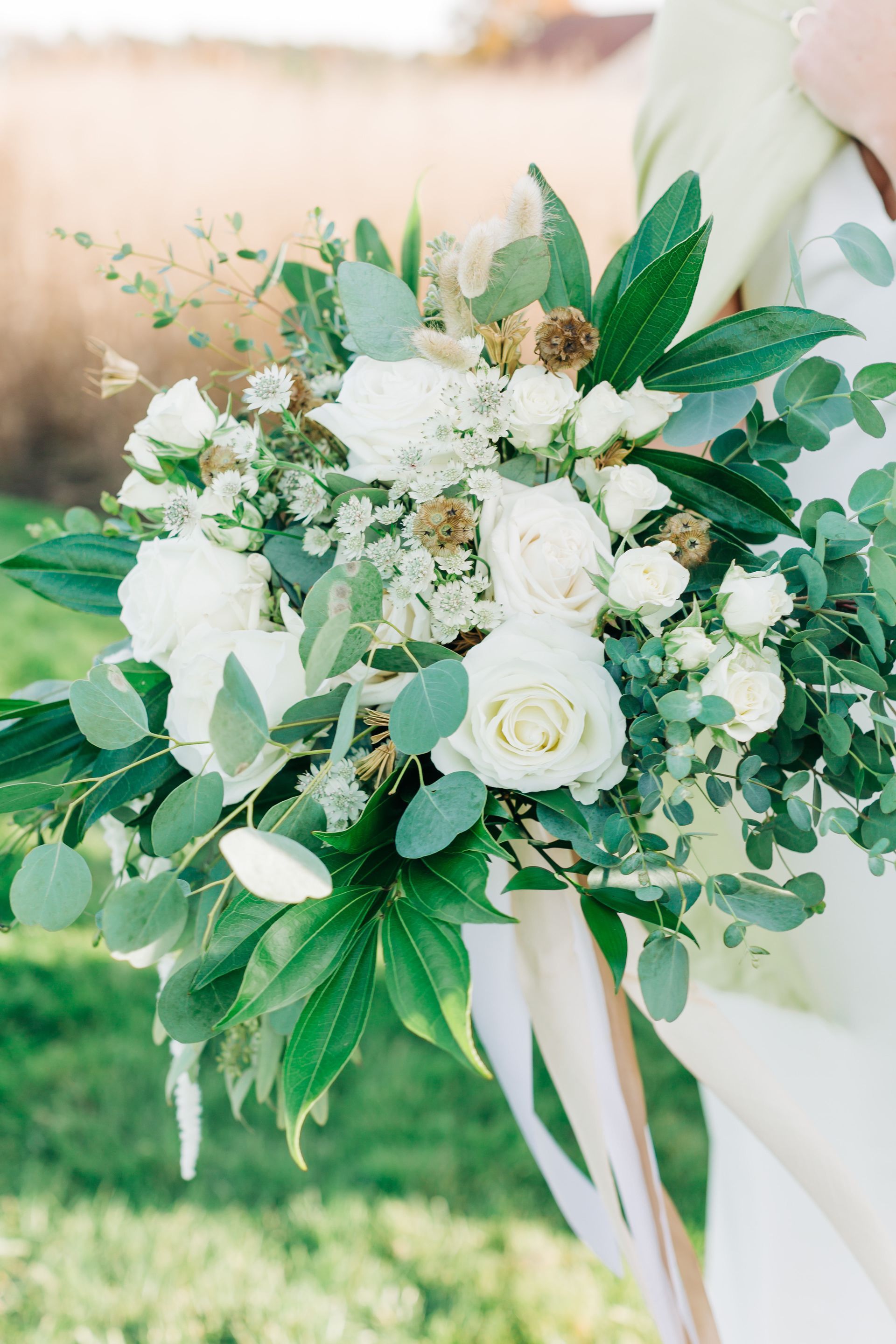 A bride is holding a bouquet of white flowers and greenery.