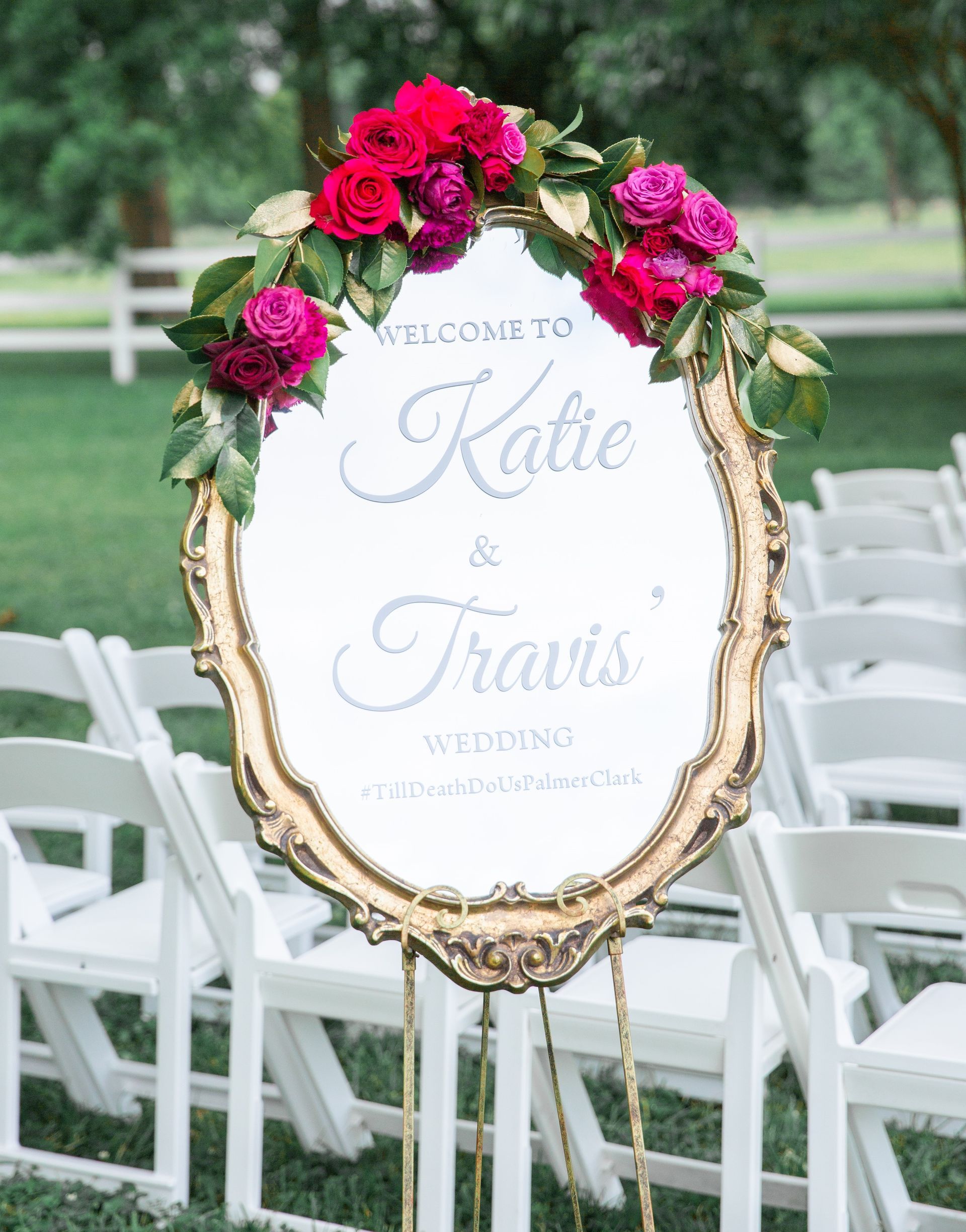 A mirror with flowers on it is sitting in front of a row of white chairs.