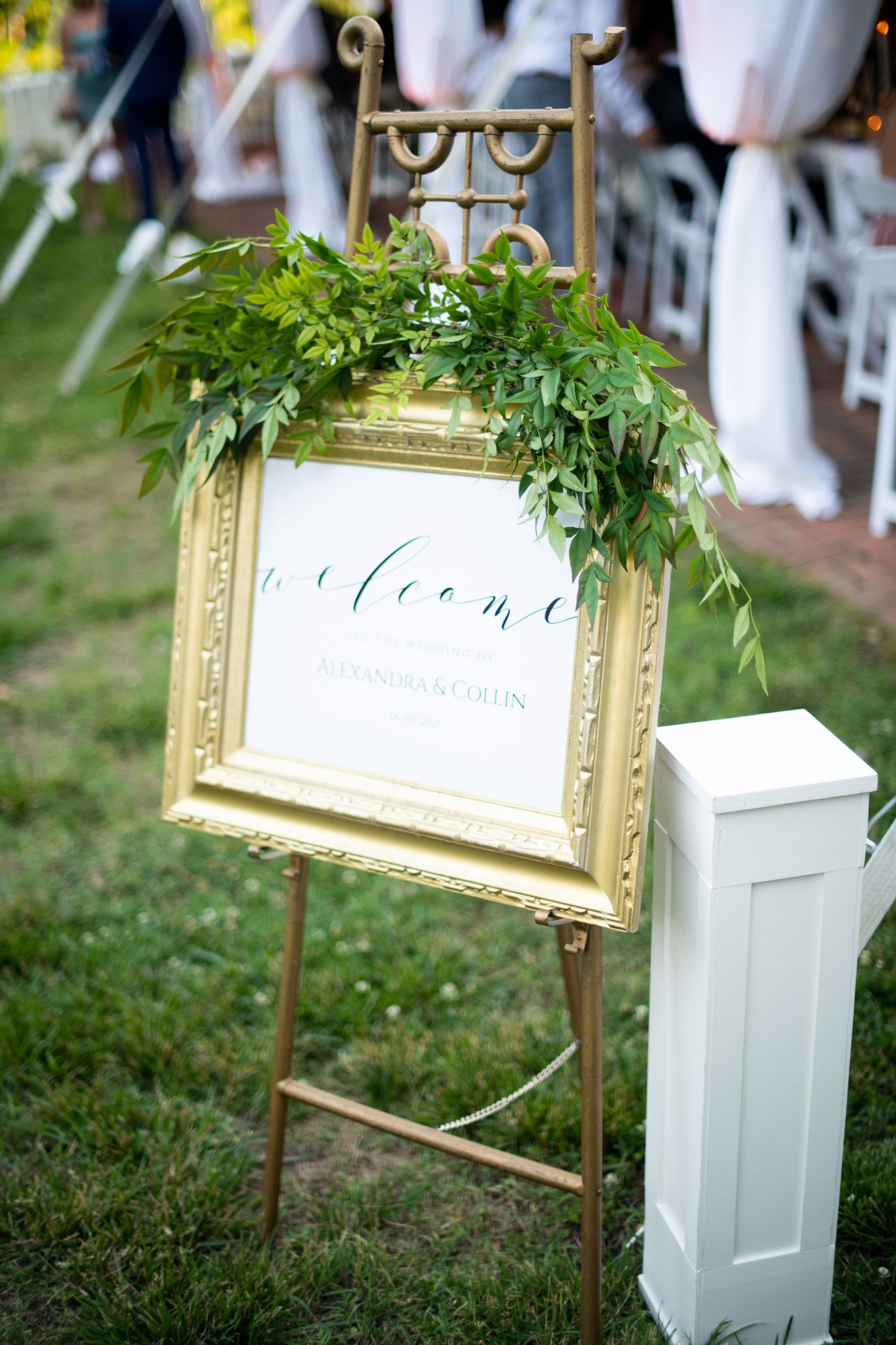A welcome sign in a gold frame is sitting on top of an easel in the grass.