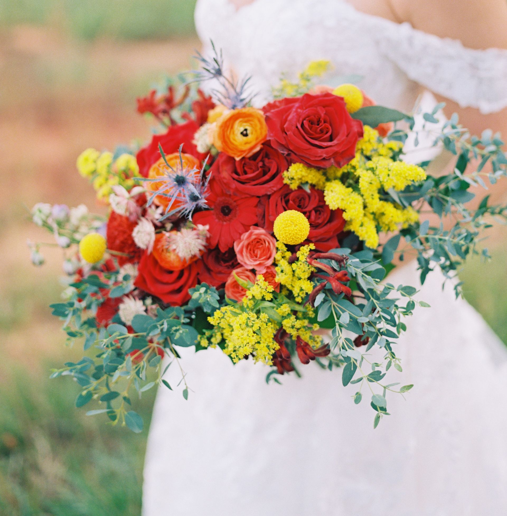 A bride in a white dress is holding a bouquet of red and yellow flowers