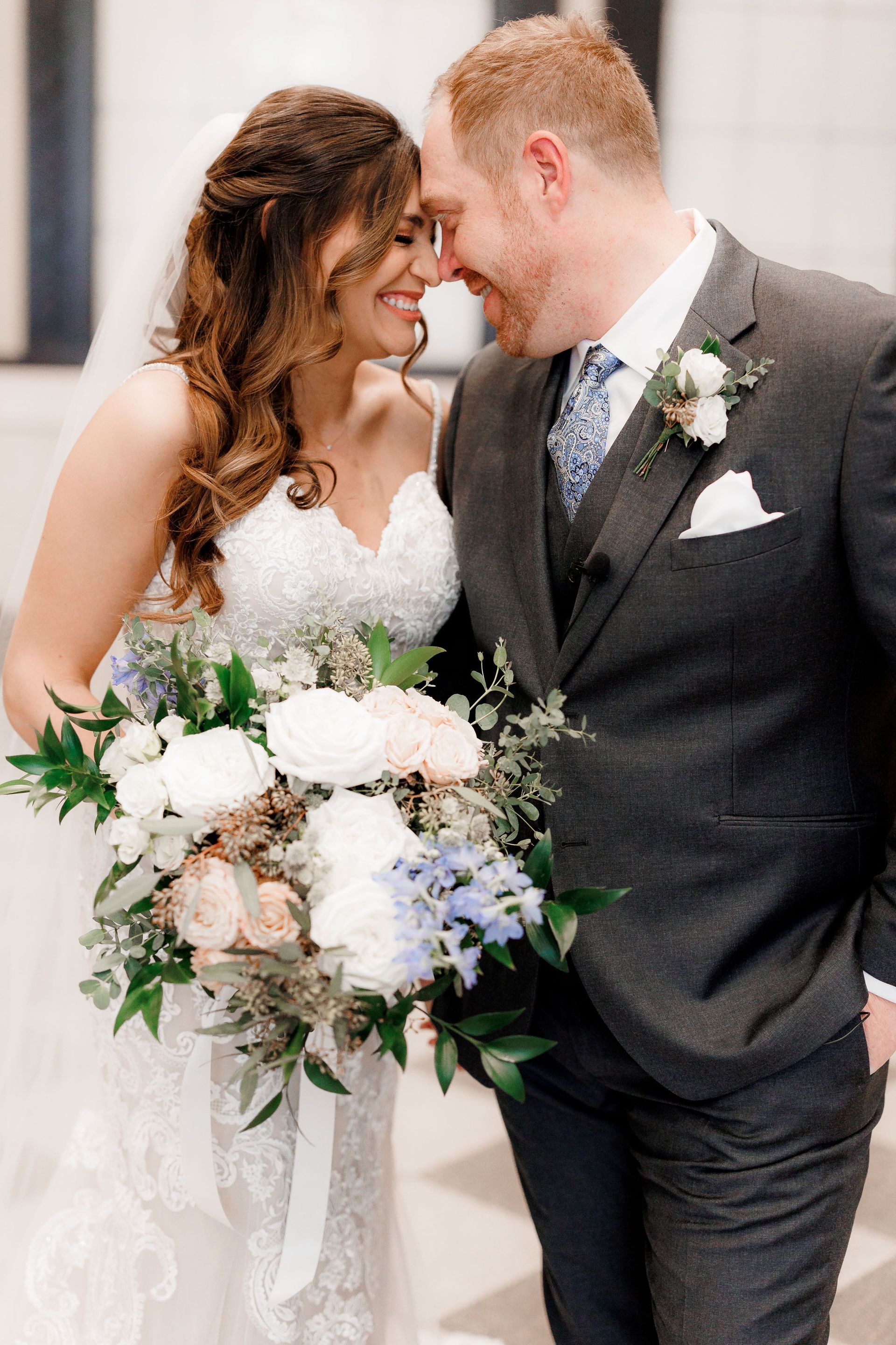 A bride and groom are looking into each other 's eyes while holding a bouquet of flowers.