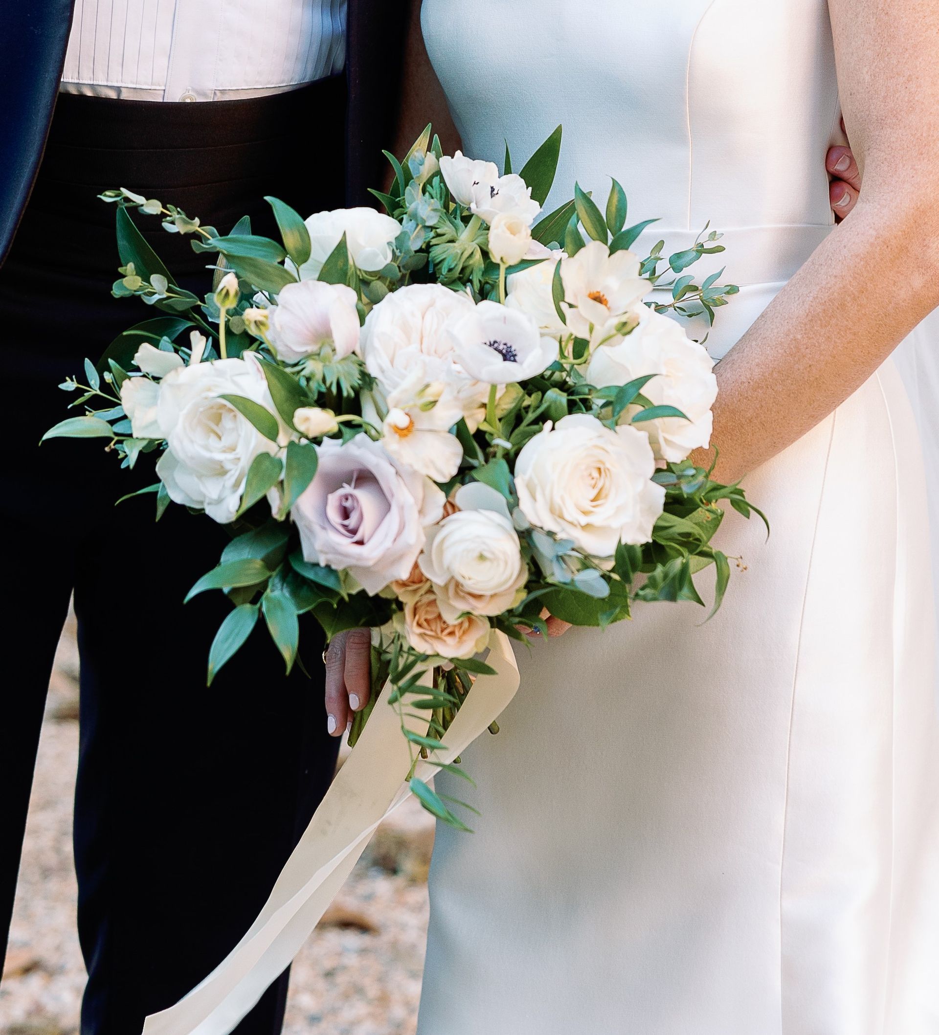 A bride in a white dress is holding a bouquet of white flowers