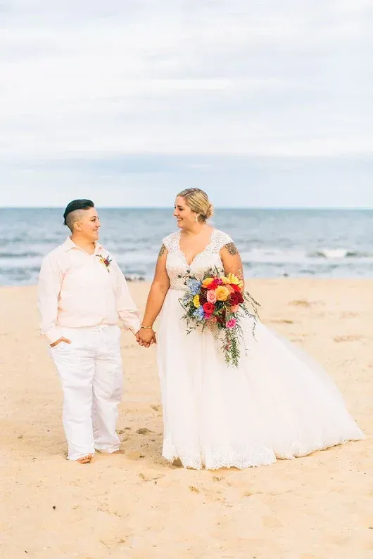 A bride and groom are holding hands on the beach.