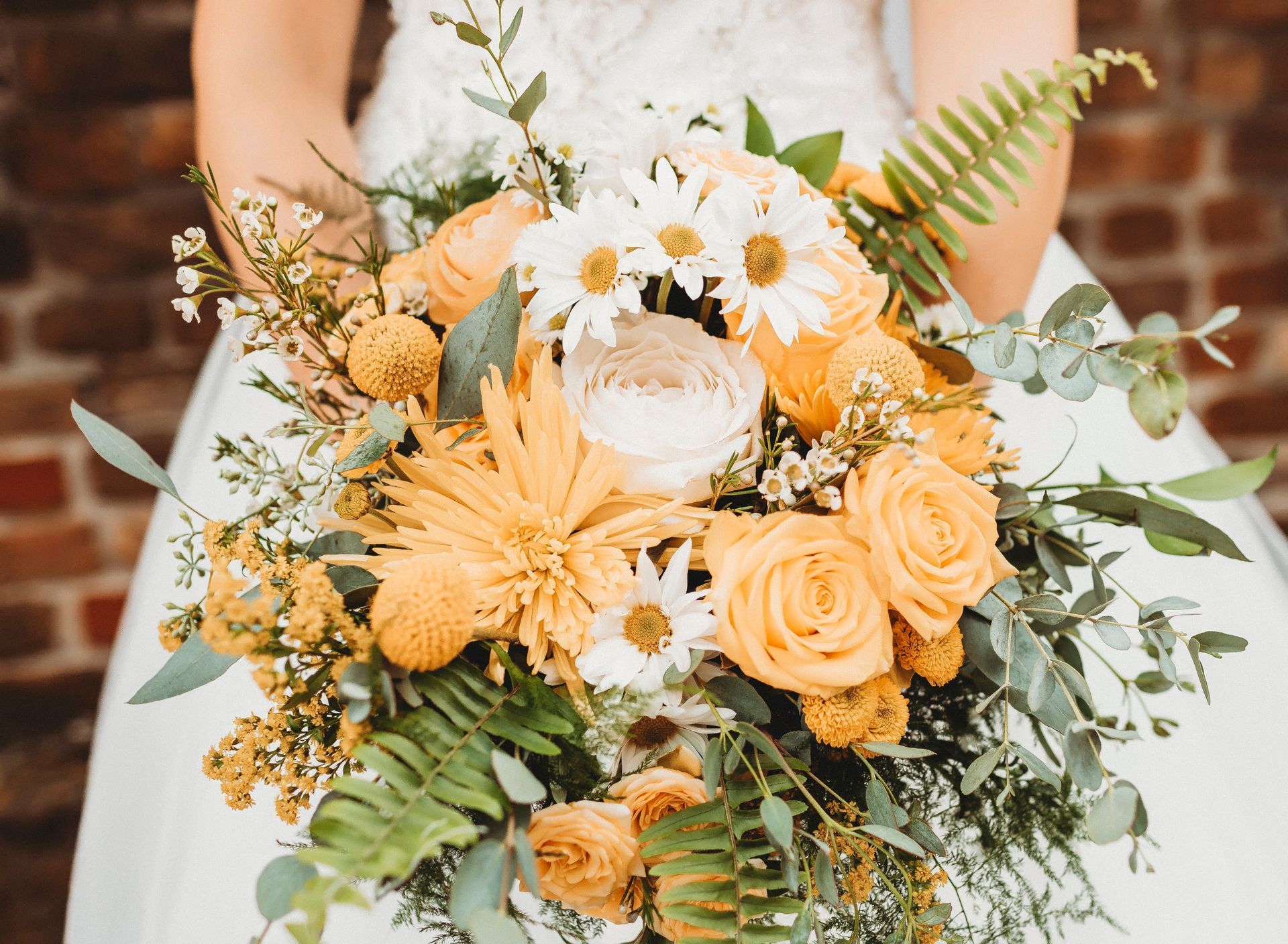 A bride in a white dress is holding a bouquet of yellow and white flowers.