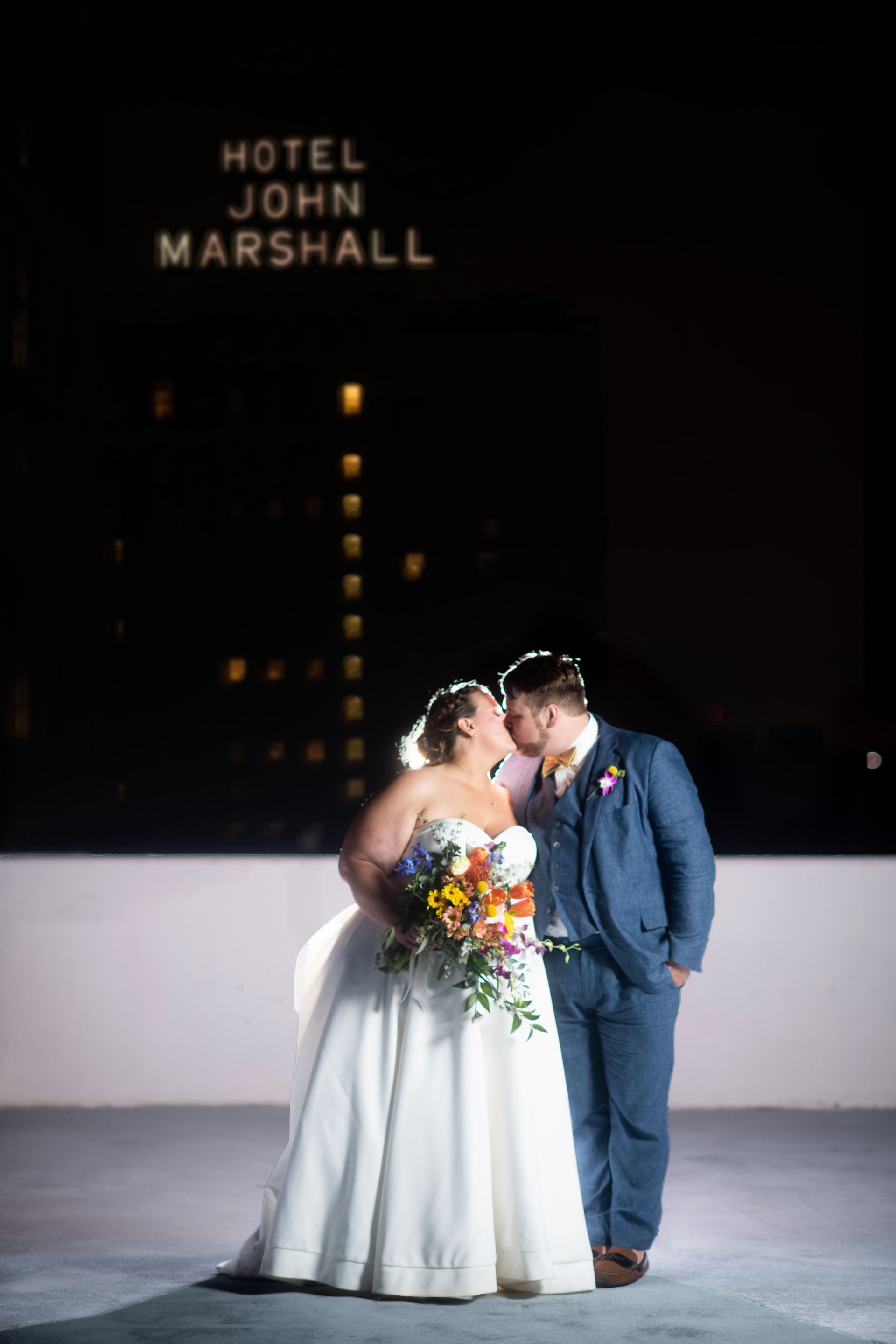 A bride and groom are kissing in front of a sign that says hotel john marshall.