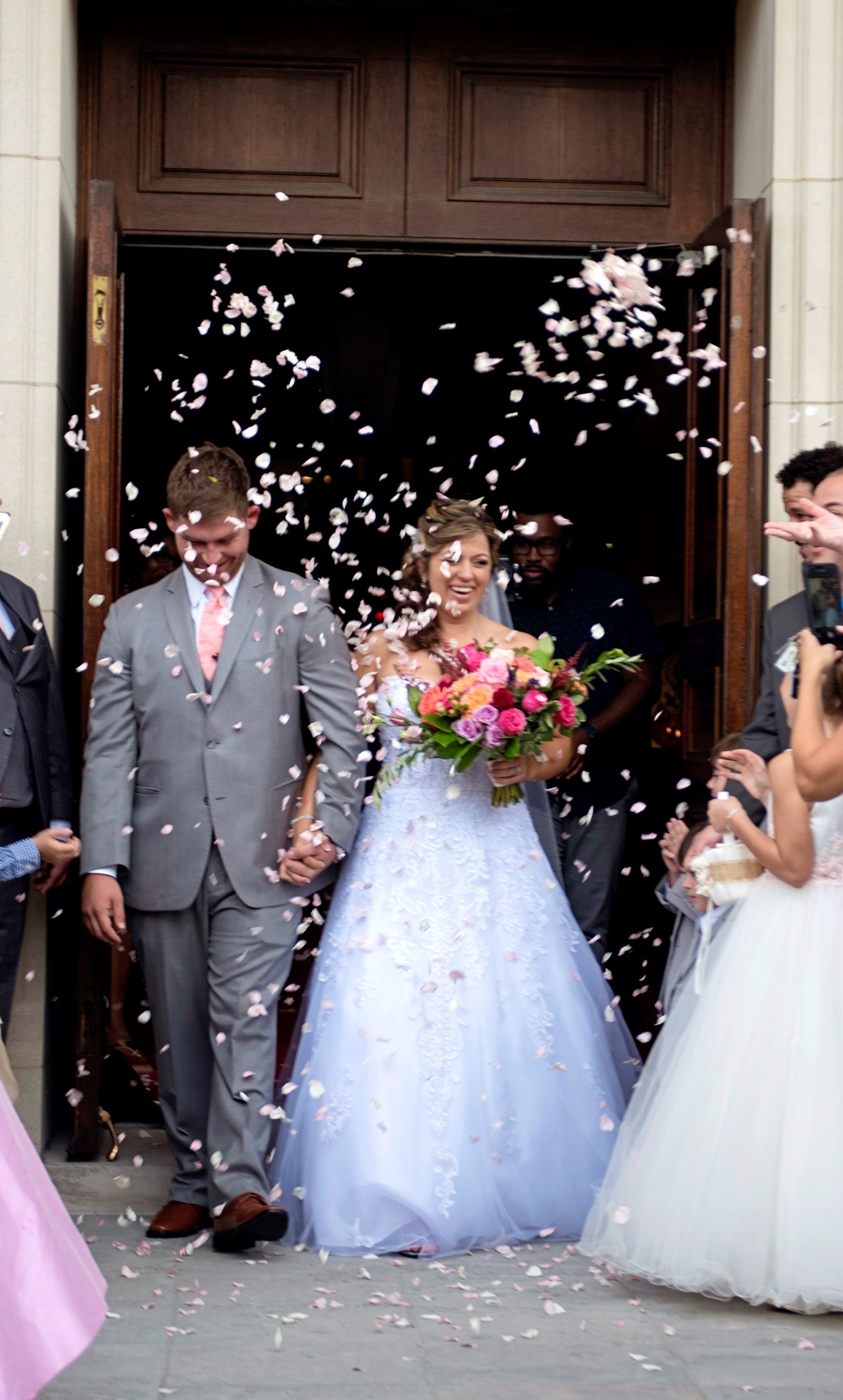 A bride and groom are walking out of a church surrounded by confetti.