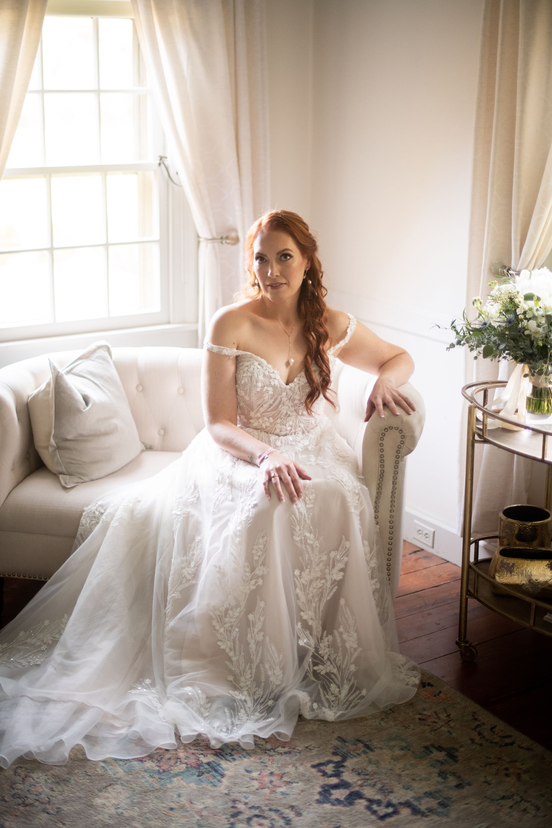 A bride in a wedding dress is sitting on a couch in front of a window.