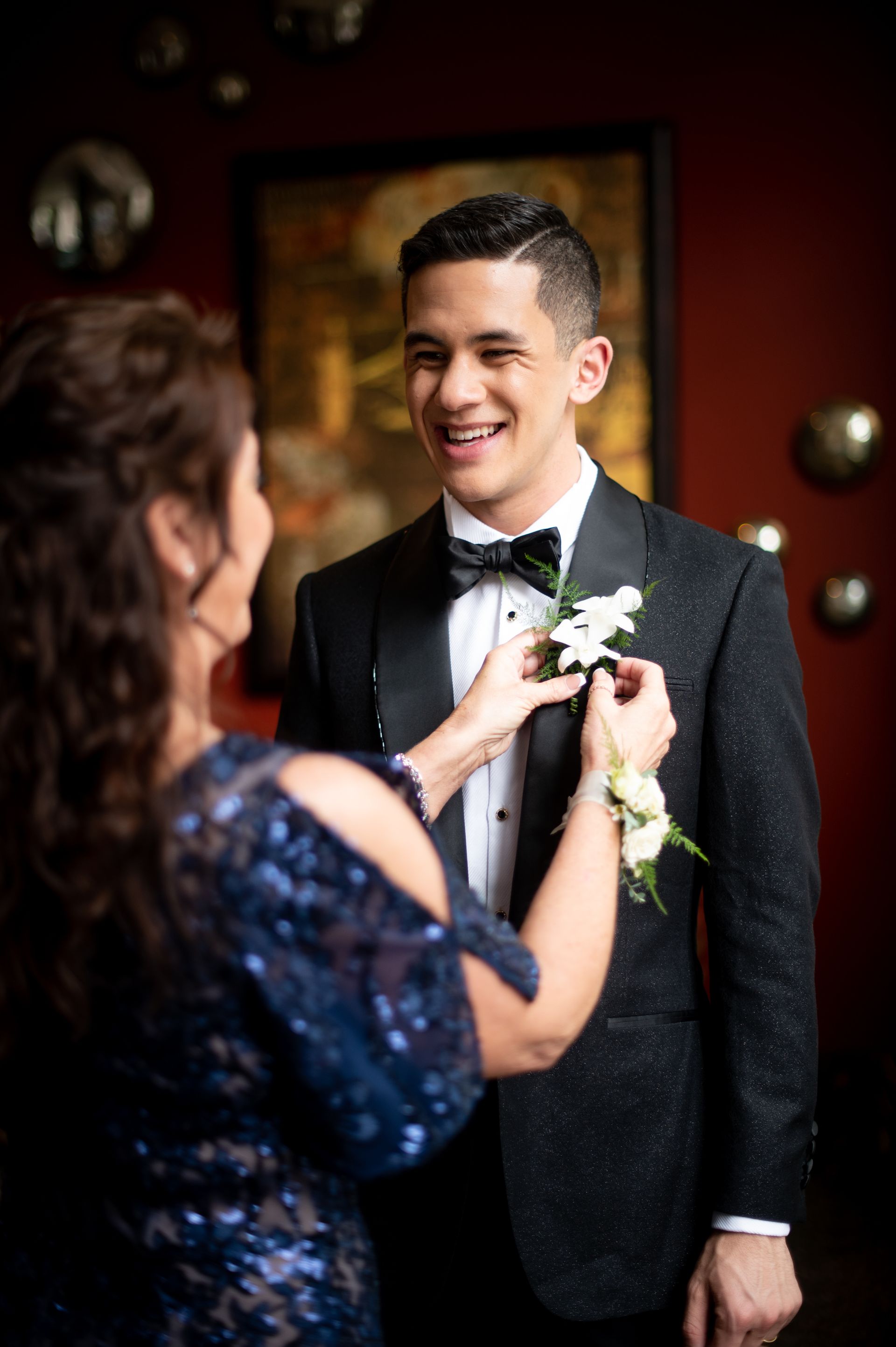 A woman is putting a flower on the lapel of a man in a tuxedo.