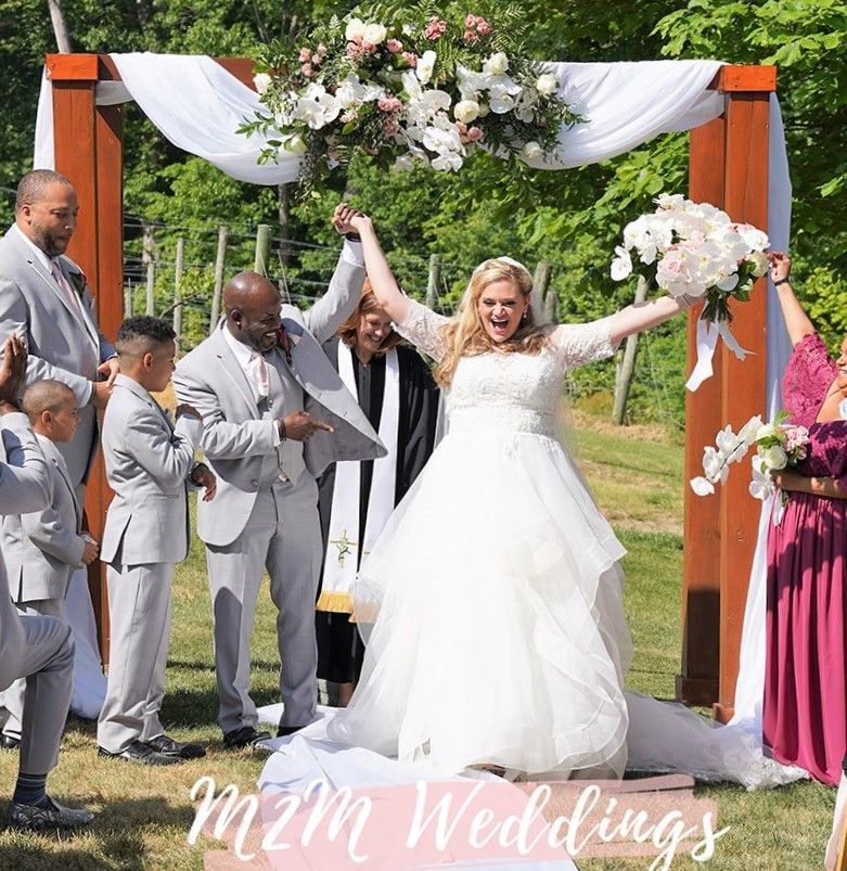 A bride and groom are celebrating their wedding under a wooden arch