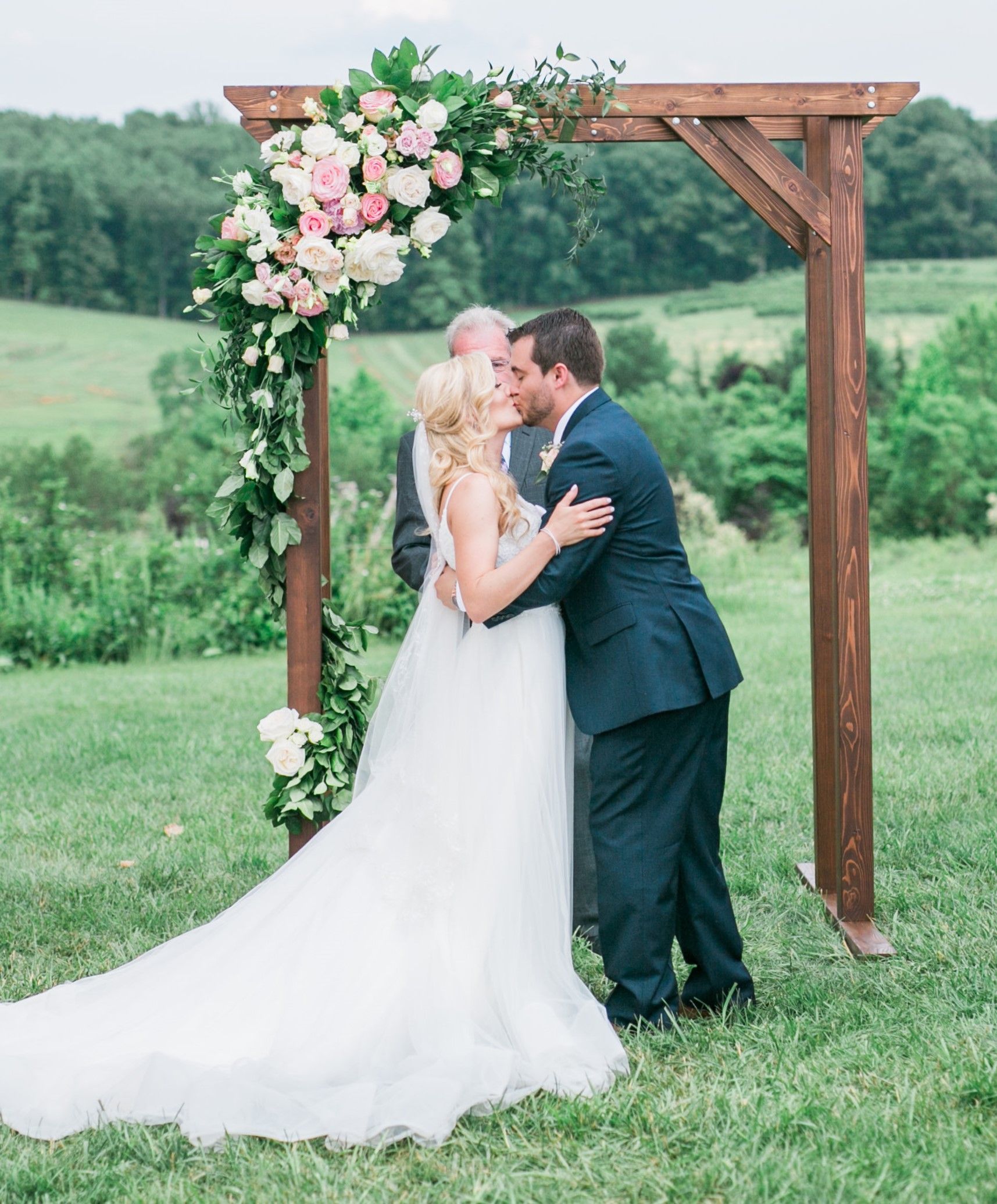 A bride and groom are kissing under a wooden arch.