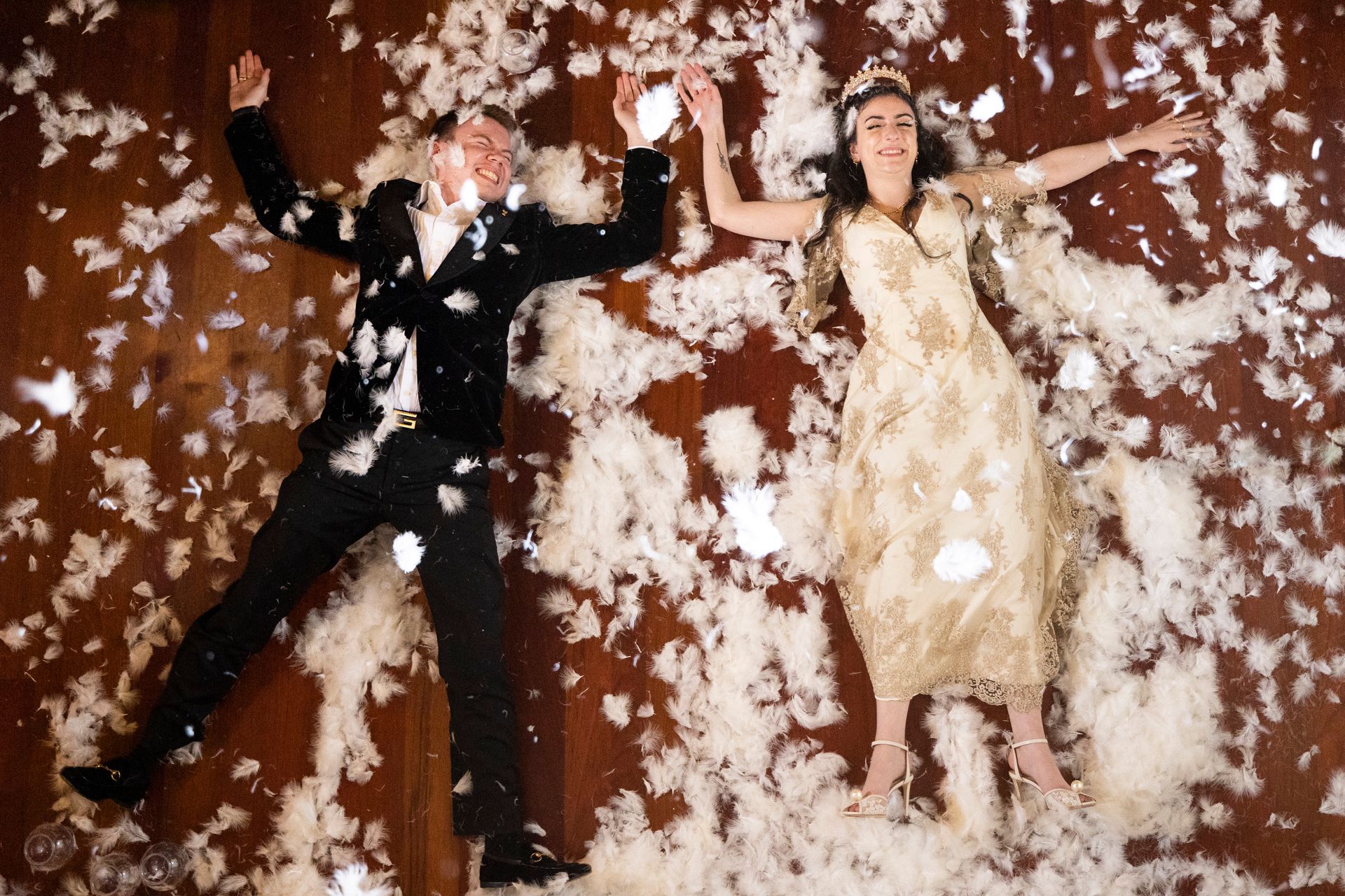 A man and a woman are laying on the floor covered in feathers.