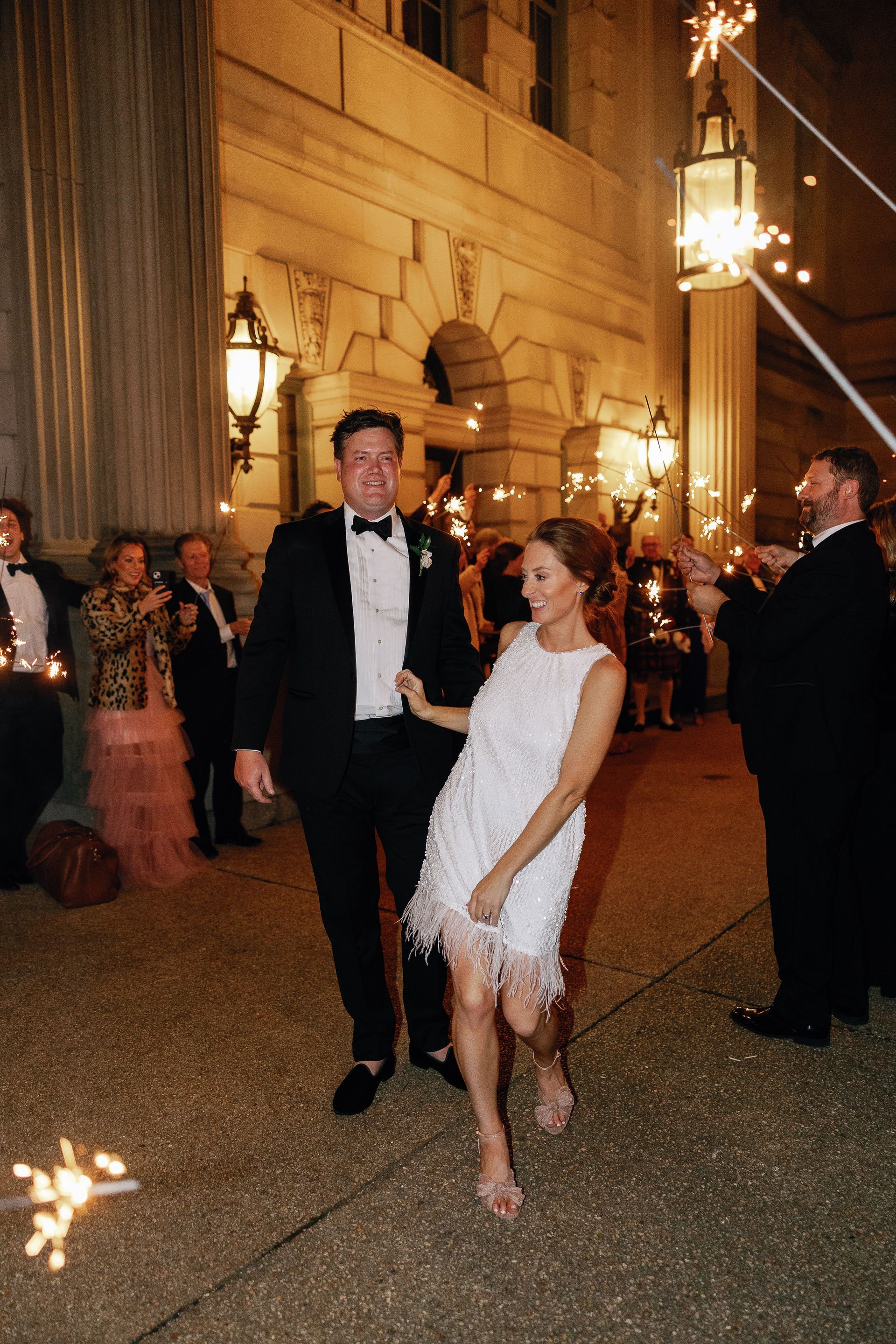 A bride and groom are walking through a crowd of people holding sparklers.