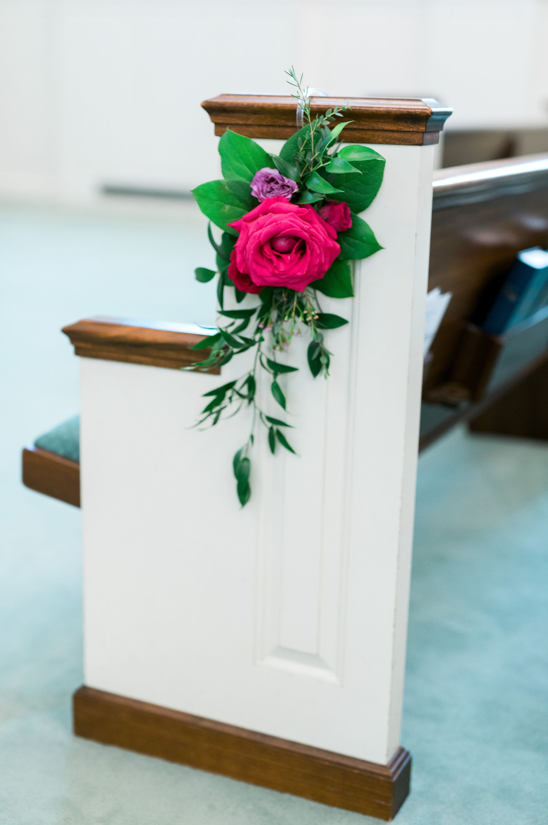 A church pew decorated with pink roses and greenery.