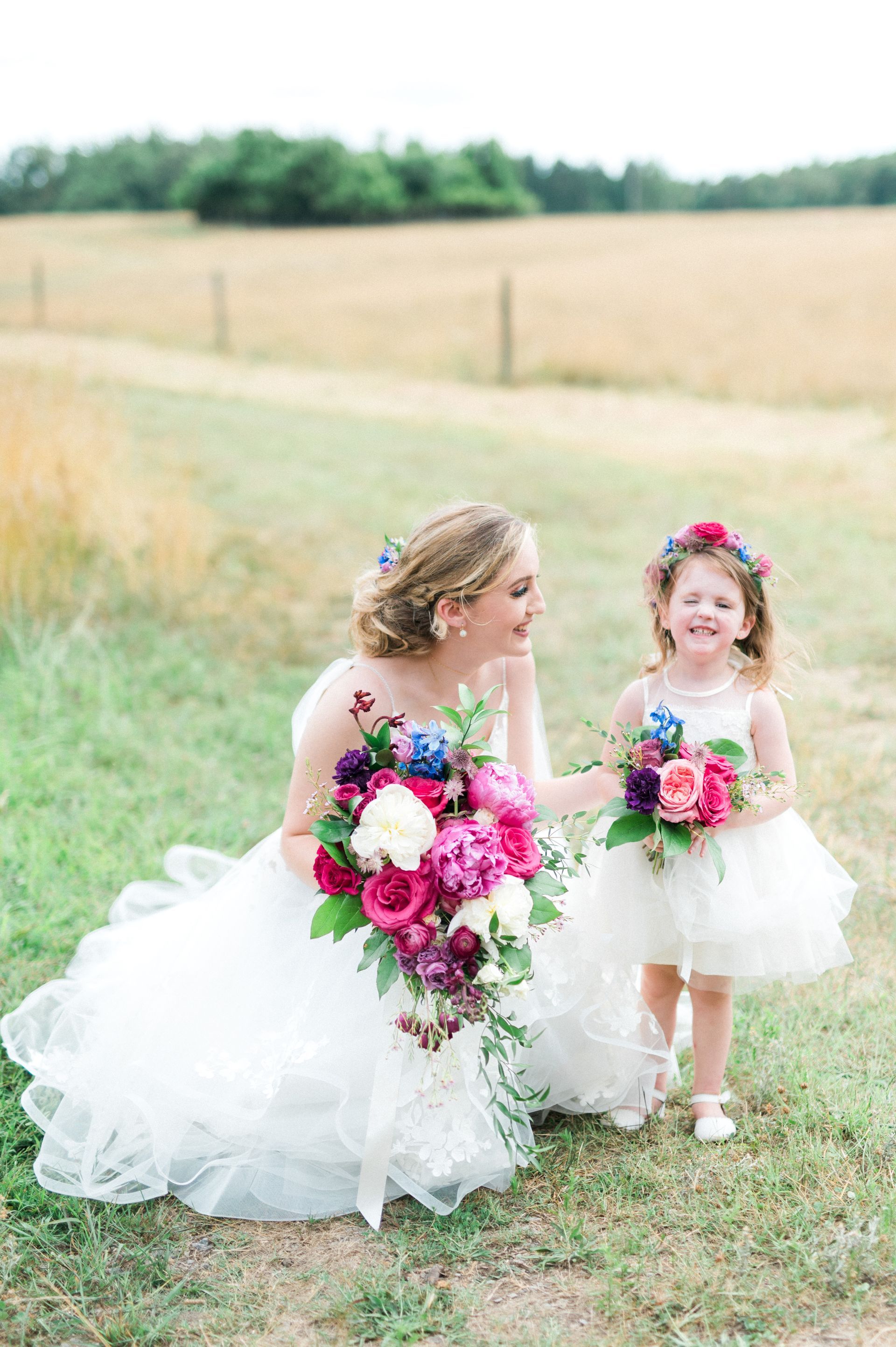 A bride and her flower girl are posing for a picture in a field.