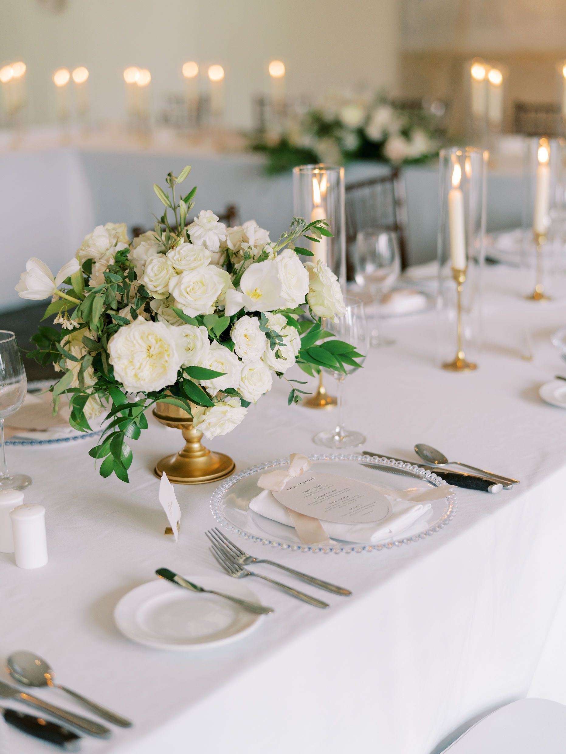 A long white table with a vase of white flowers on it.