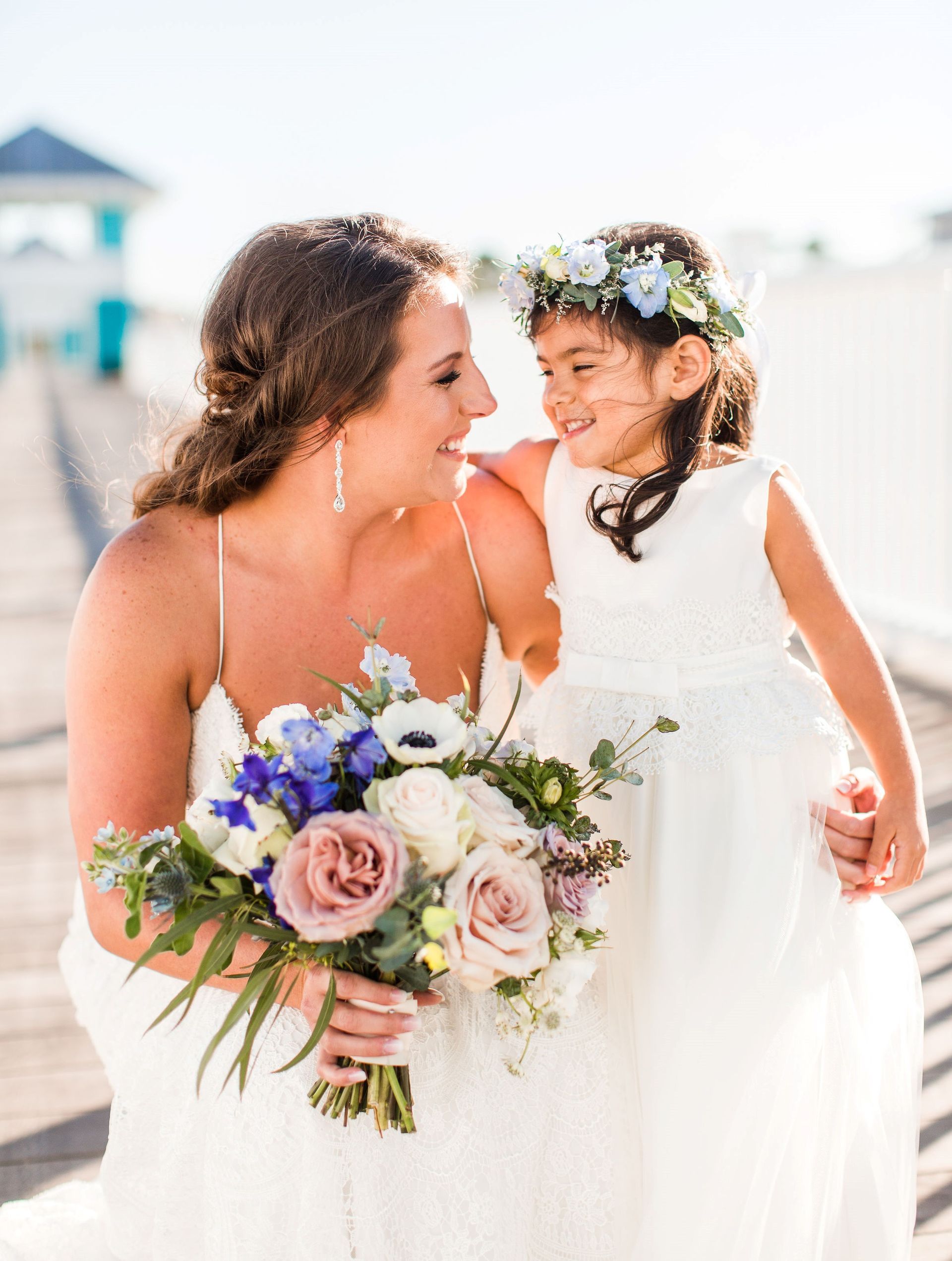 A bride and her flower girl are standing next to each other on a dock.