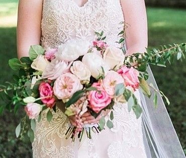 A bride in a wedding dress is holding a bouquet of pink flowers.