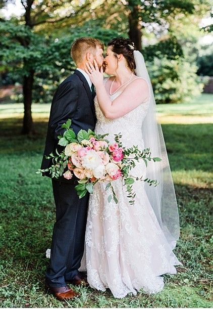 A bride and groom are kissing in a park while holding a bouquet of flowers.
