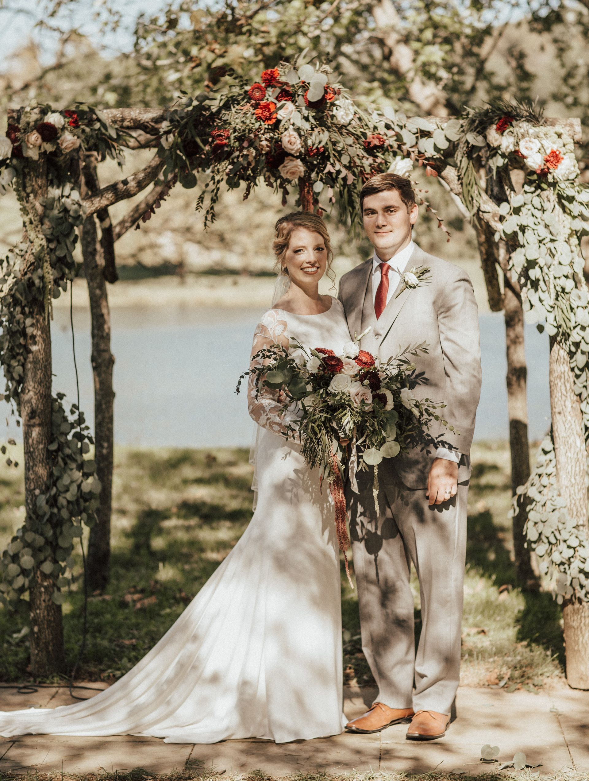 A bride and groom are posing for a picture under a wooden arch.