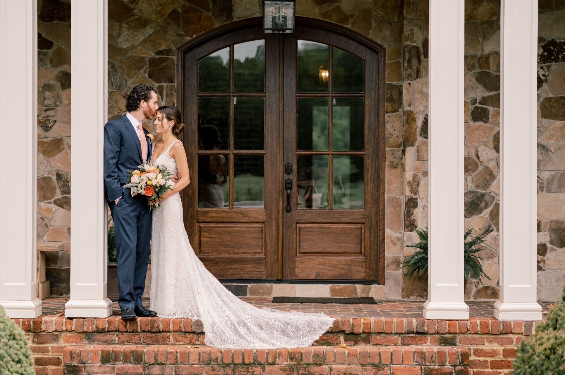 A bride and groom are posing for a picture on the steps of a house.