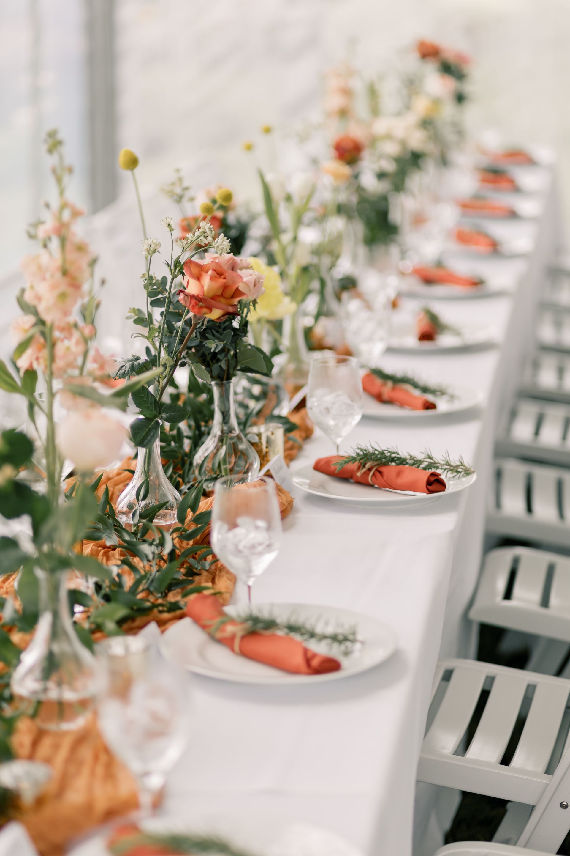 A long table with plates , glasses , and flowers on it.