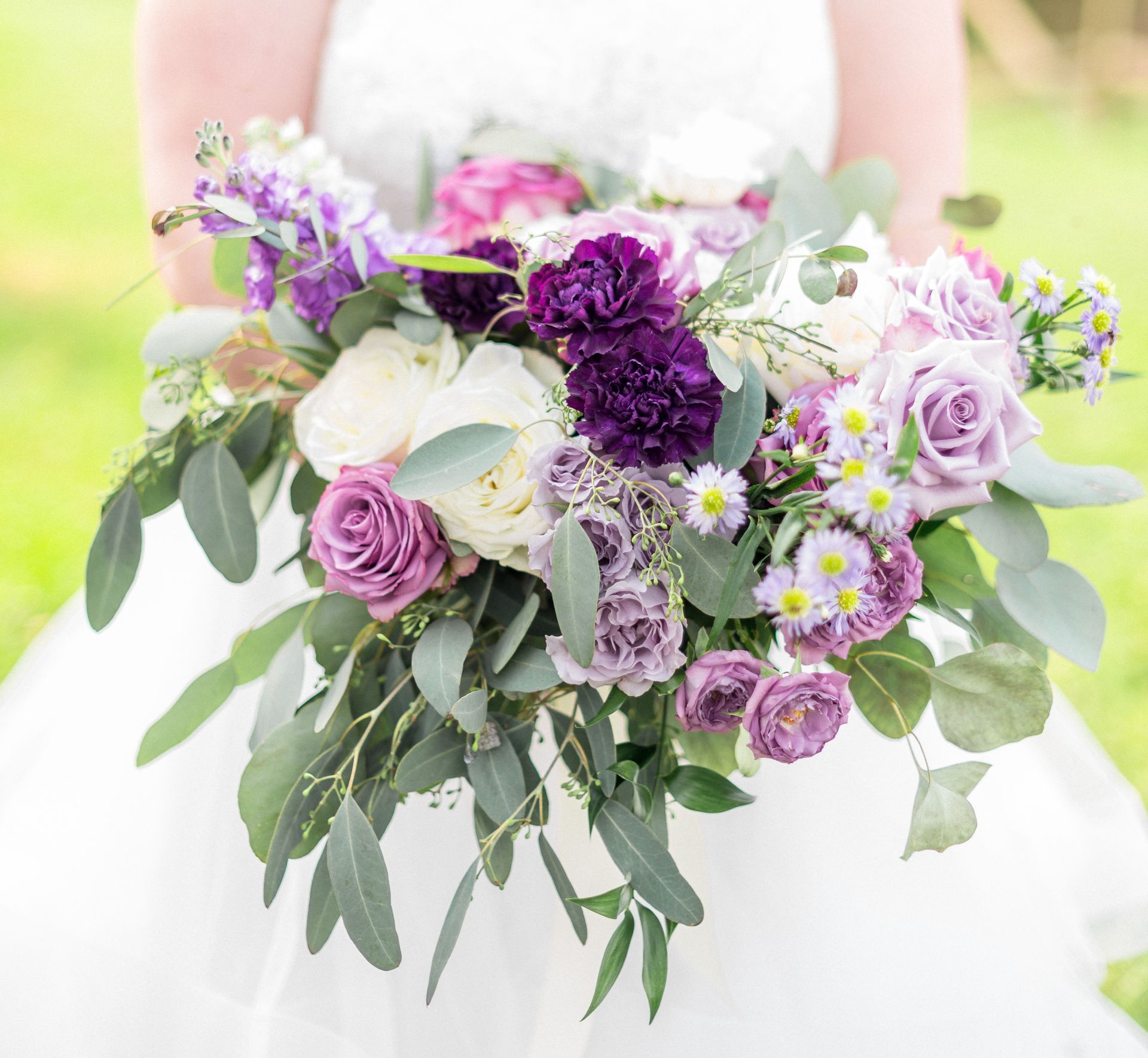 A bride in a white dress is holding a bouquet of purple and white flowers.