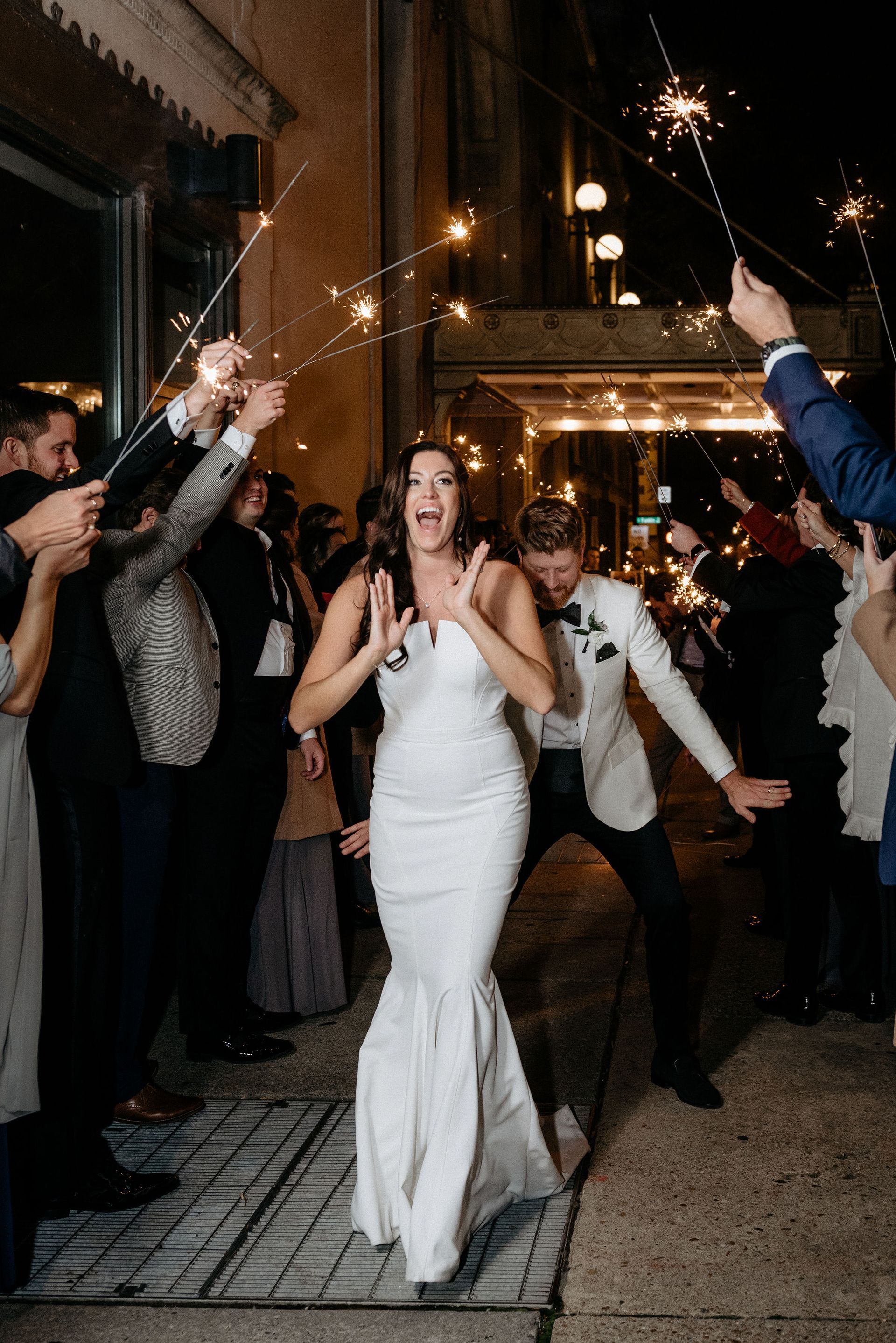 A bride and groom are walking through a crowd of people holding sparklers.