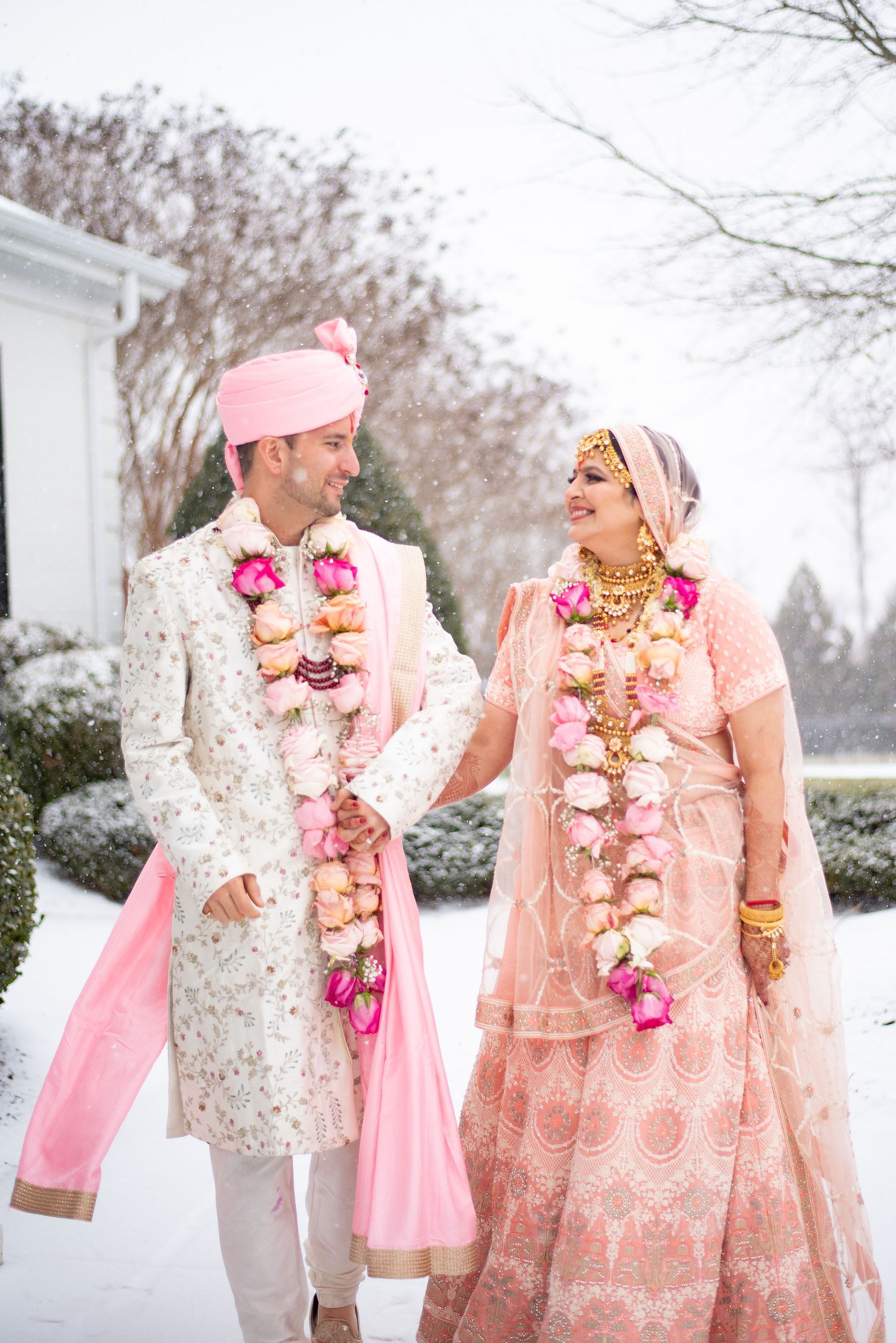 A bride and groom are walking in the snow holding hands.