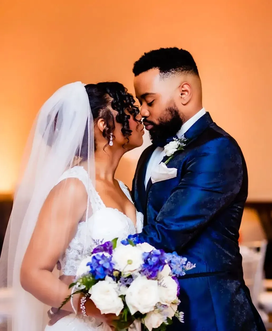 A bride and groom are kissing while holding a bouquet of flowers.