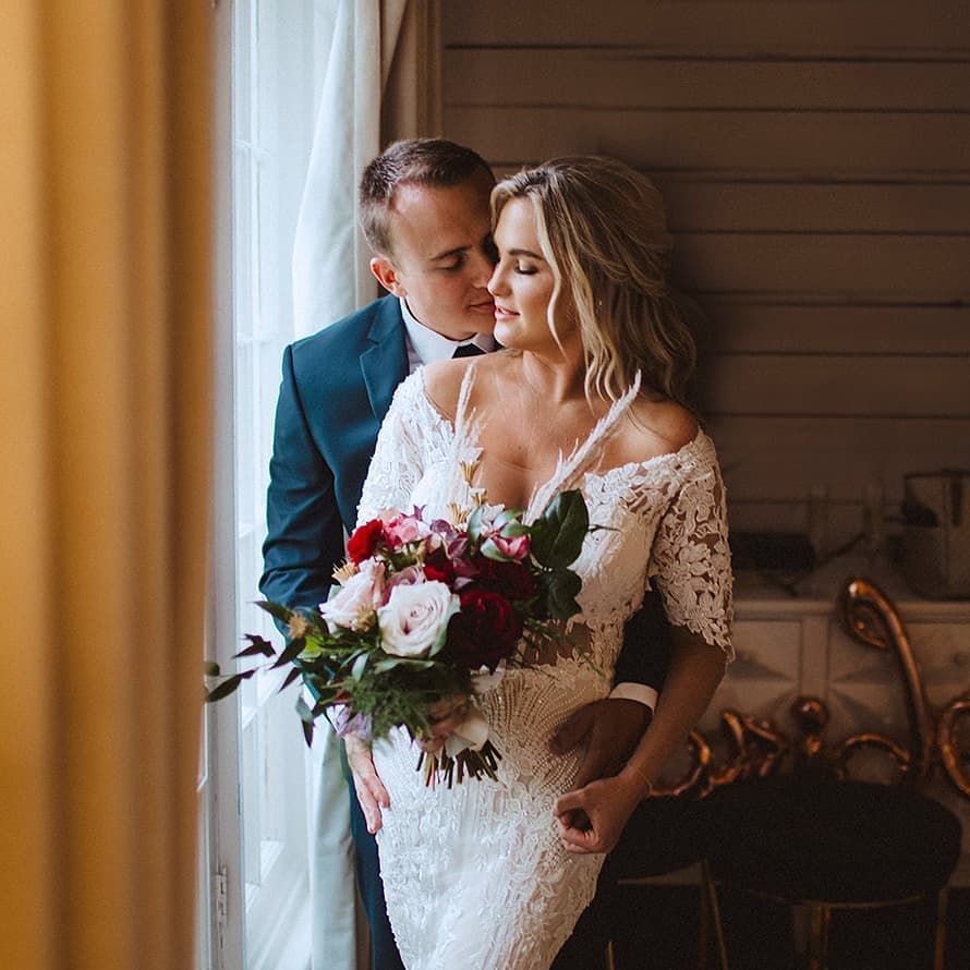 A bride and groom are posing for a picture in front of a window.