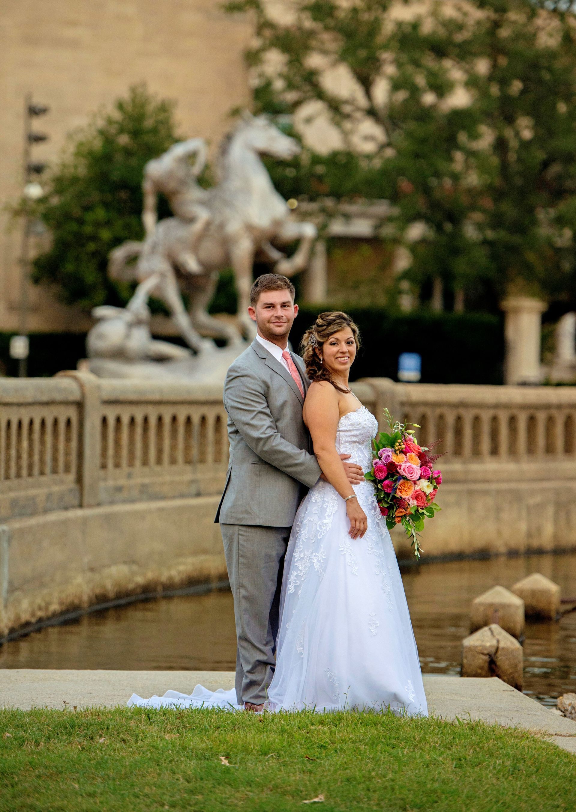 A bride and groom are posing for a picture in front of a statue of a horse.