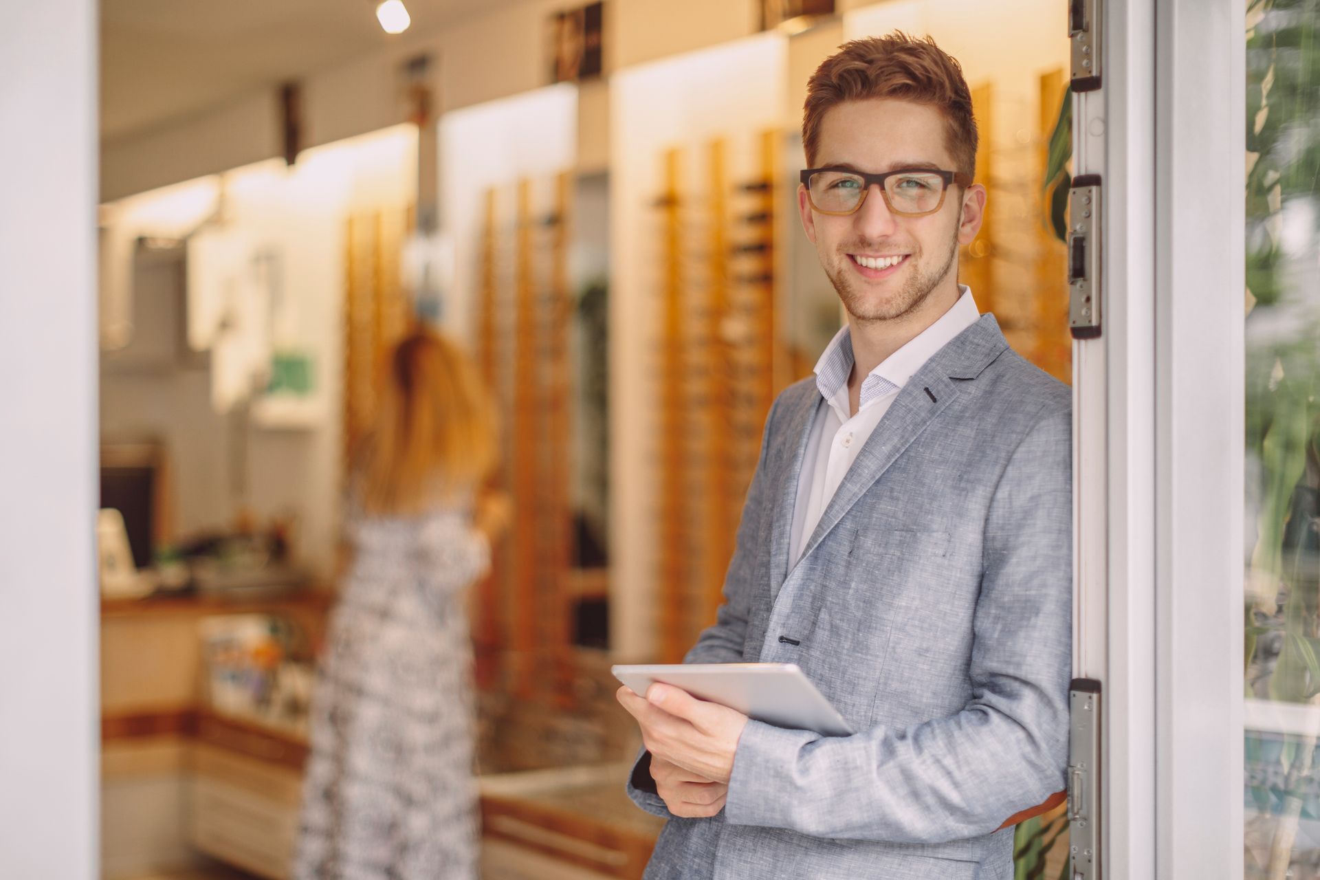 A man in a suit and glasses is standing in a doorway holding a tablet.