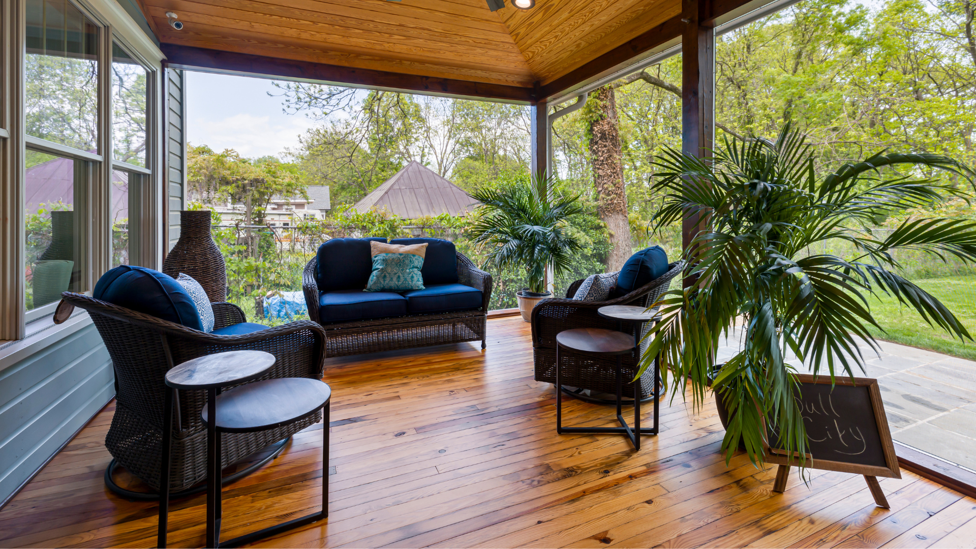A screened in porch with a couch , chairs , tables and a potted plant.
