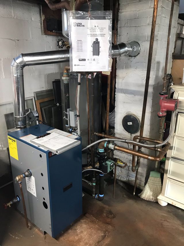 Boiler room with blue and white HVAC equipment, exposed pipes, and concrete walls, with water on the floor