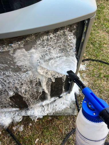 Spraying white foam cleaner onto a dirty outdoor appliance grille with a blue nozzle