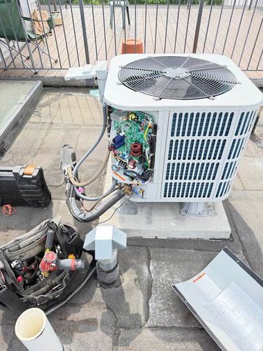 Outdoor HVAC unit with open side panel and exposed wiring beside tools on a concrete patio