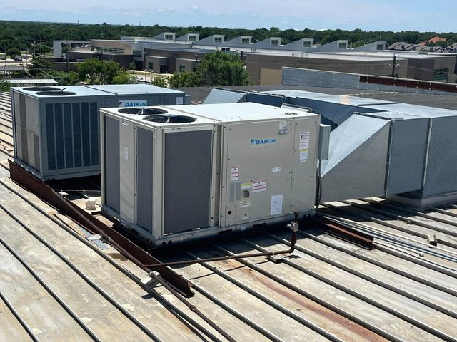 Row of large rooftop HVAC units on a metal roof under a clear sky