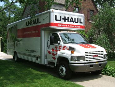U-Haul moving truck parked on a driveway in front of a house. White truck with red accents.