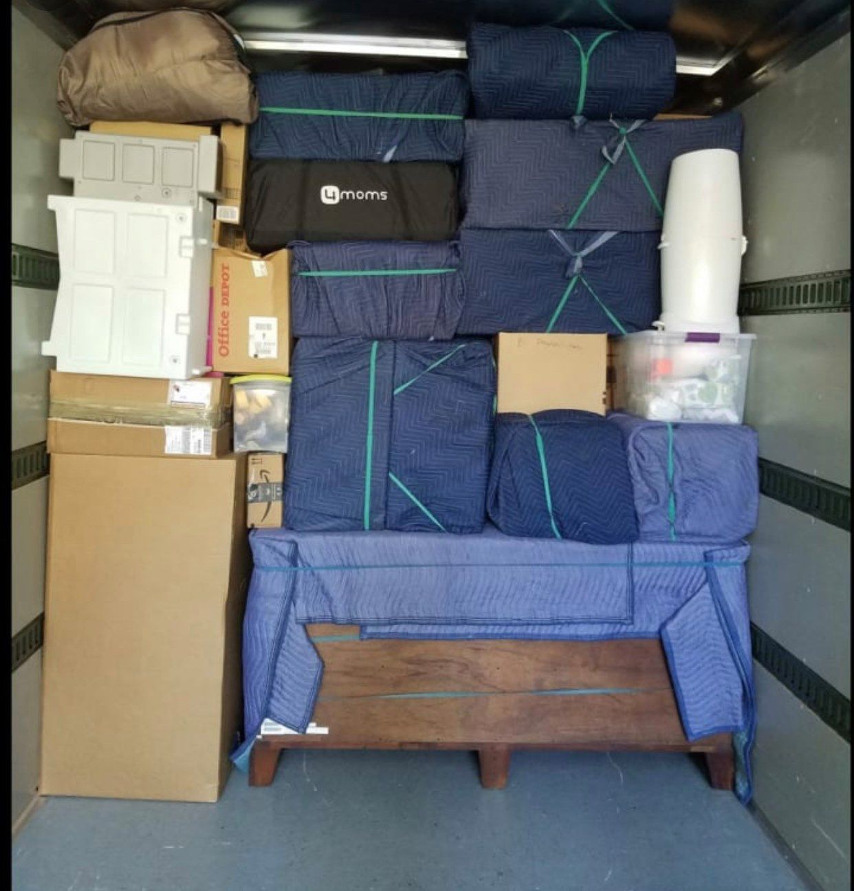 A packed moving truck interior, stacked with furniture, boxes, and various items wrapped in blue padding.