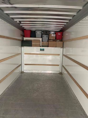 Inside of a moving truck with several boxes and bins on a shelf in the back.
