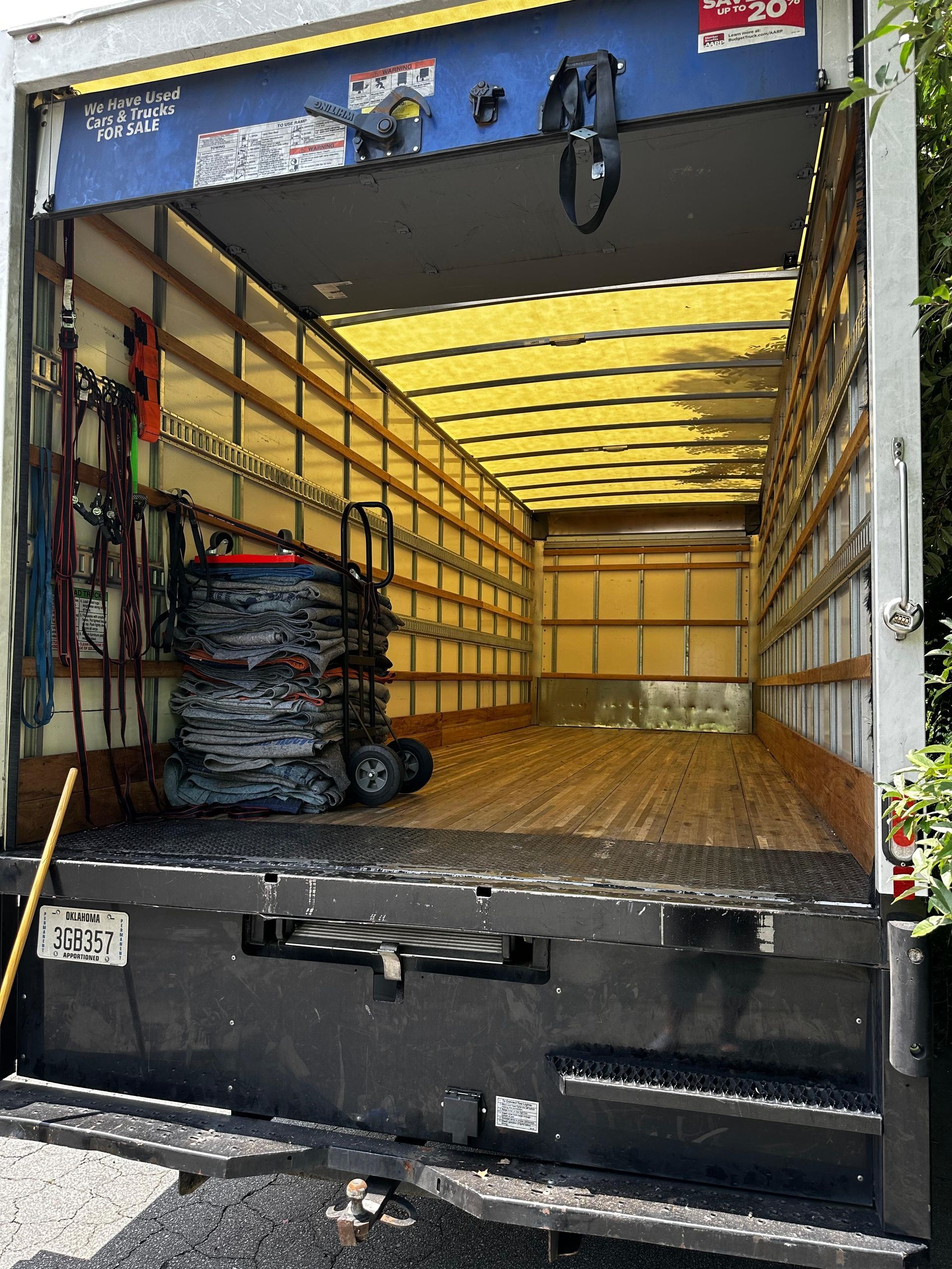 Inside of an empty moving truck with a liftgate down. Black liftgate, wooden floors, and yellow ceiling.