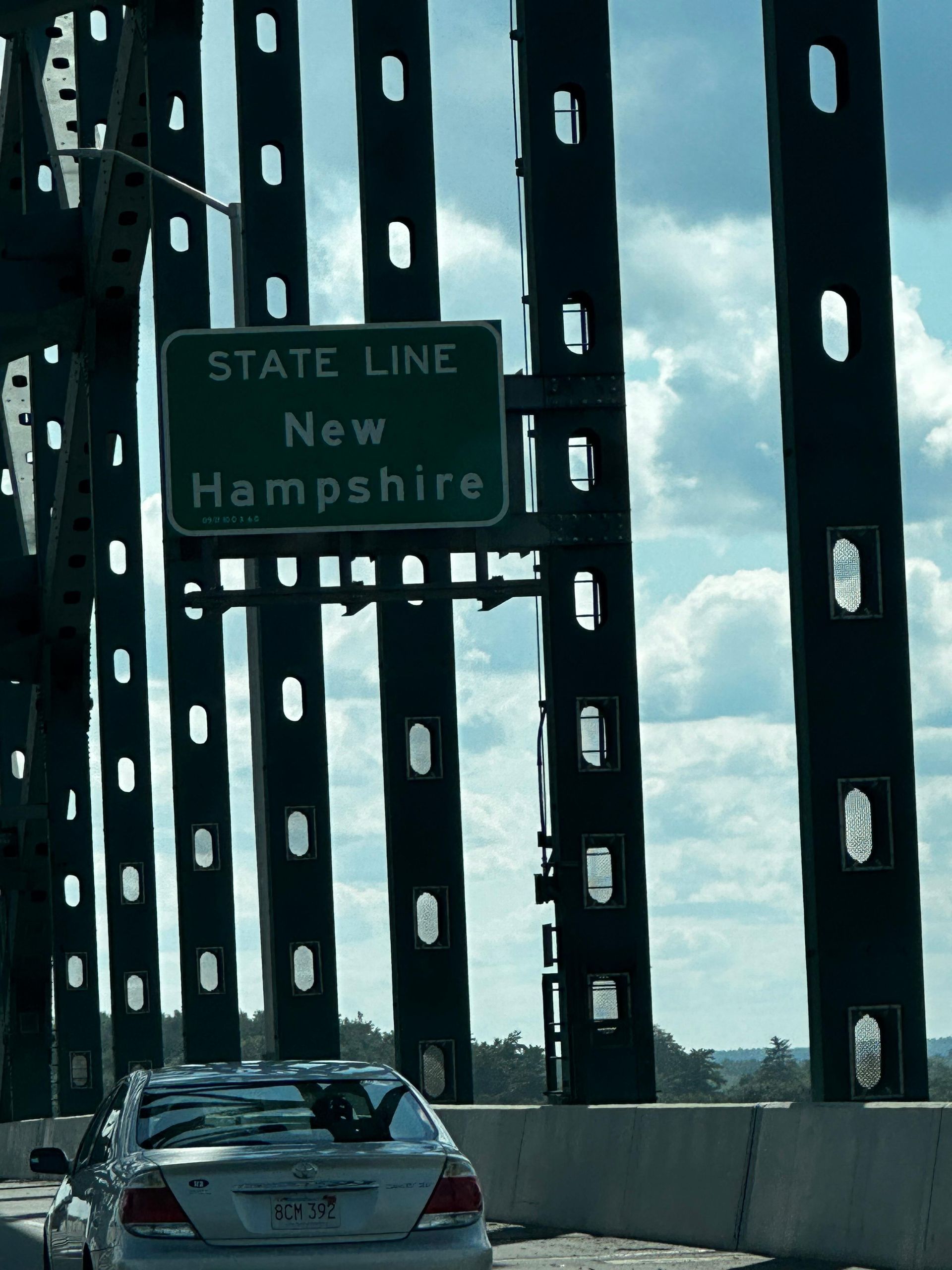 A car crosses a bridge into New Hampshire. A green sign says 