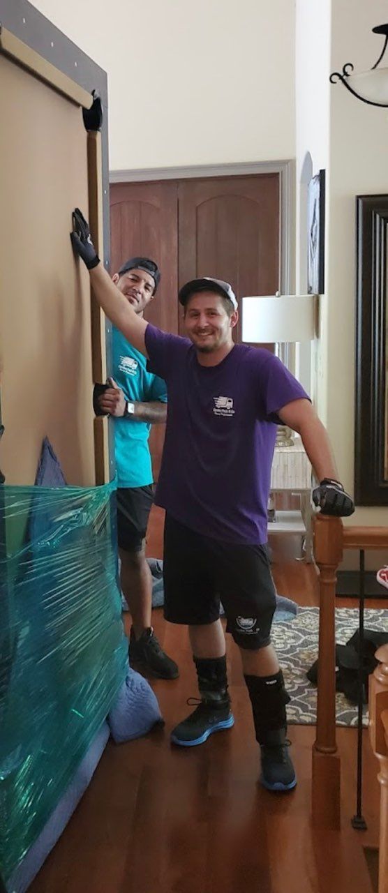 Two movers lifting a wrapped item inside a home. One raises his arm smiling.